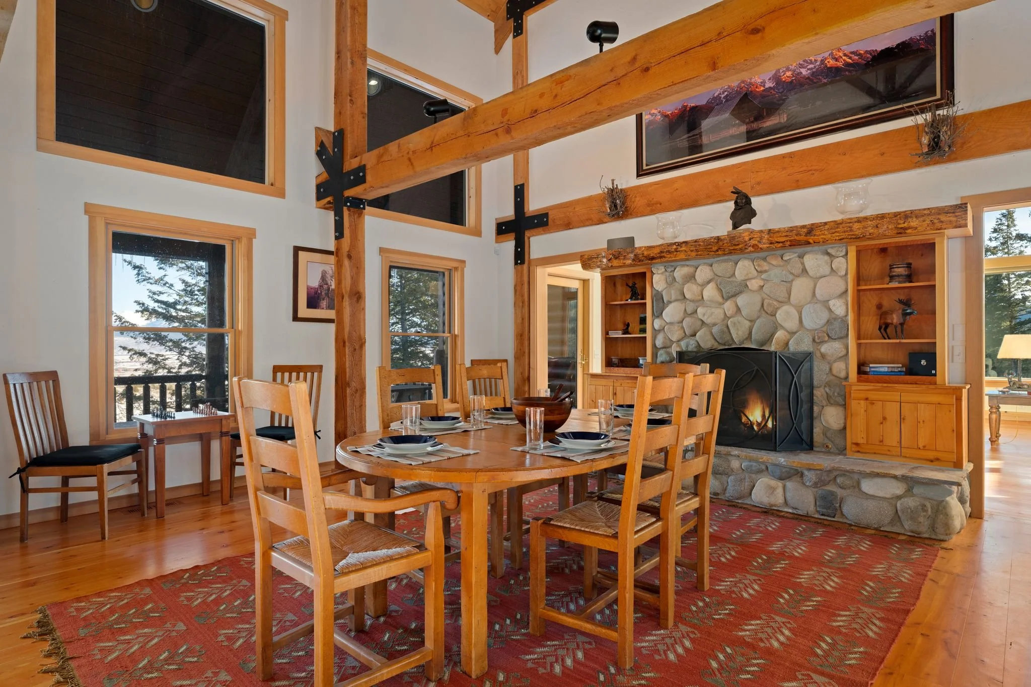 Rustic dining room with wooden beams, stone fireplace, and a round wooden table with chairs.