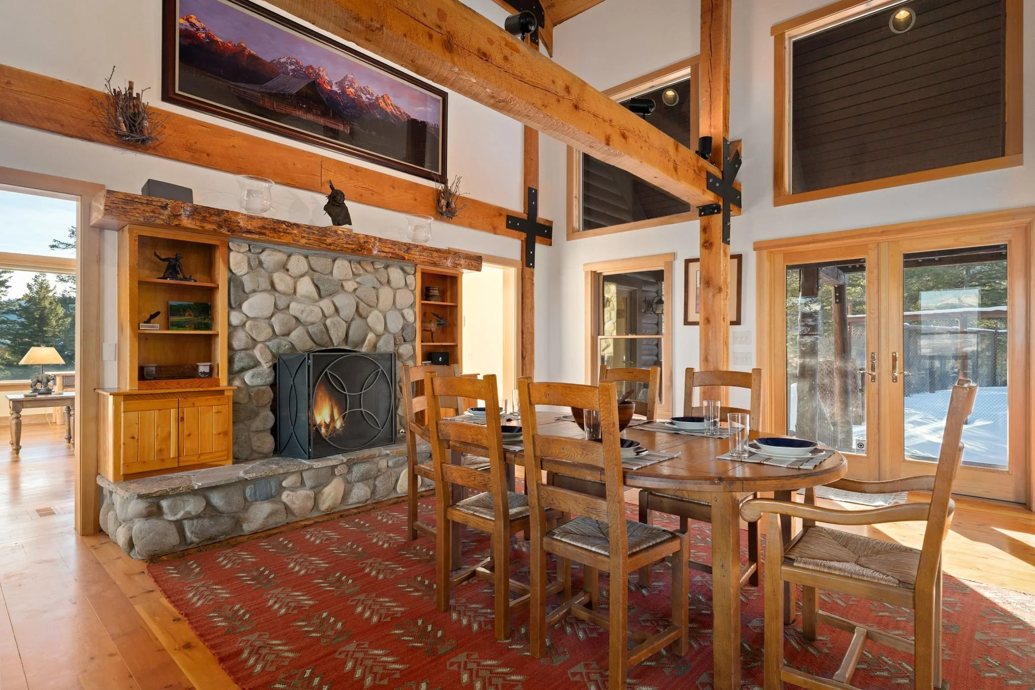 Dining room with wooden furniture, a stone fireplace, wall art, windows, and a glass door leading outside.