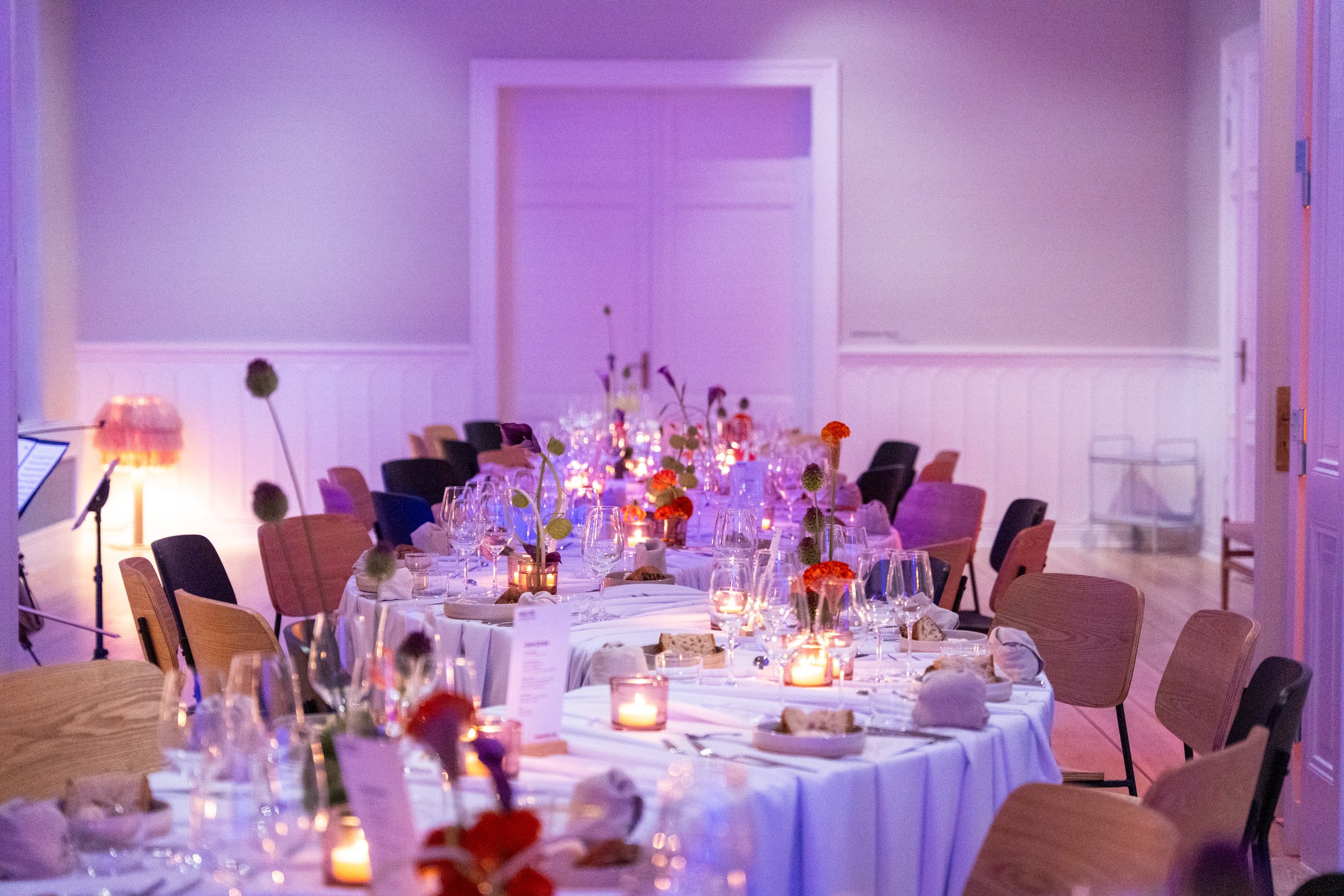 Ein eleganter Festtisch mit weißen Tischtüchern, Kerzen, Gläsern und bunten Blumenarrangements in der festlich dekorierten Location.