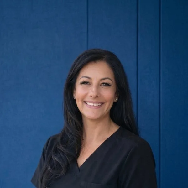 Dr. Valencia with dark hair smiling against a blue background.