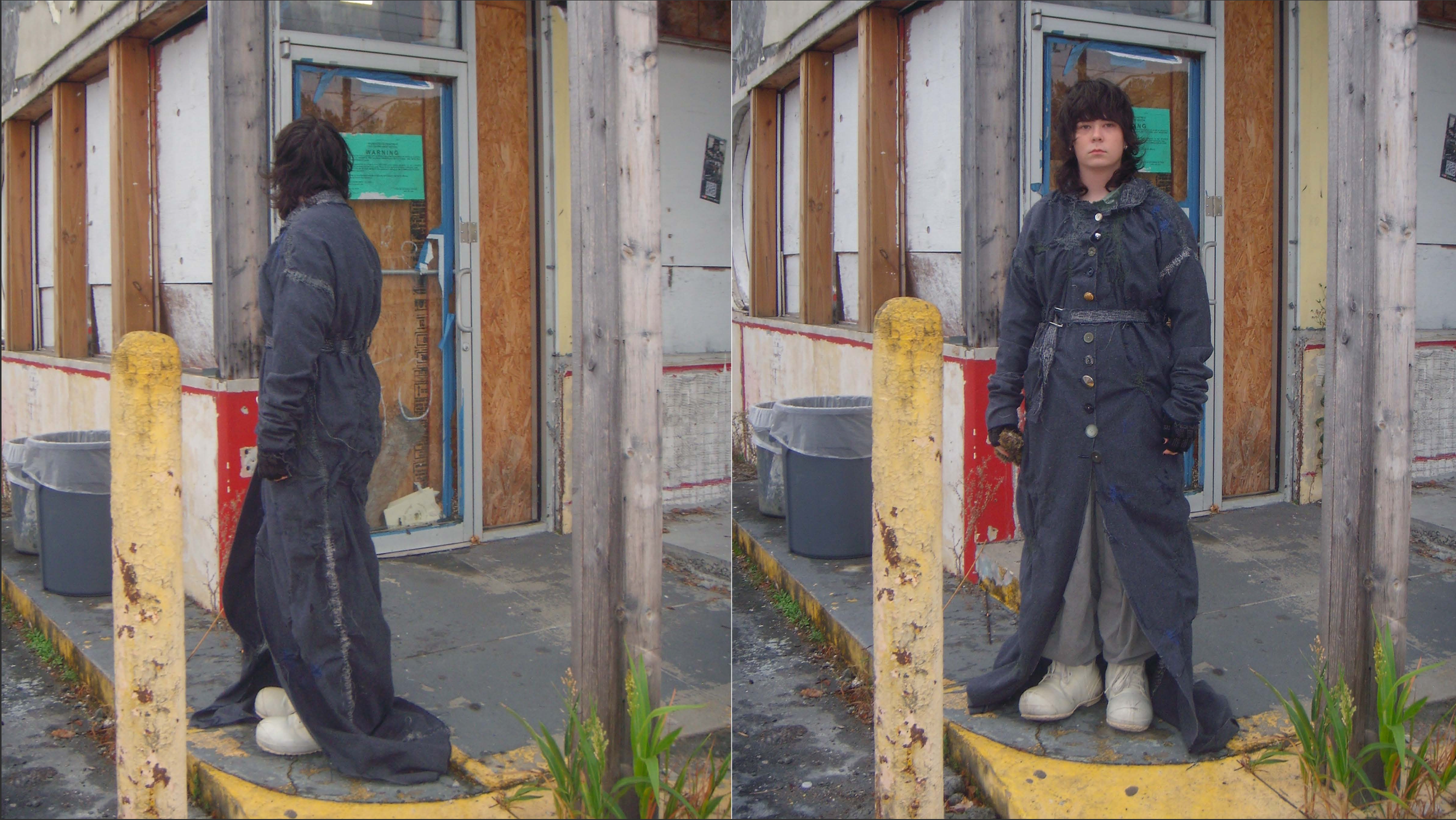 A young  with dark, curly hair wearing an oversized, dark coat with large buttons, standing on a yellow curb outside a building under renovation. The building has exposed wood framing and plywood, with a blue door and a green warning sign. She is hol