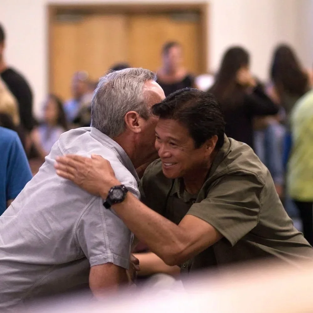Two men imbracing in joy as others in their support group are in the boackground