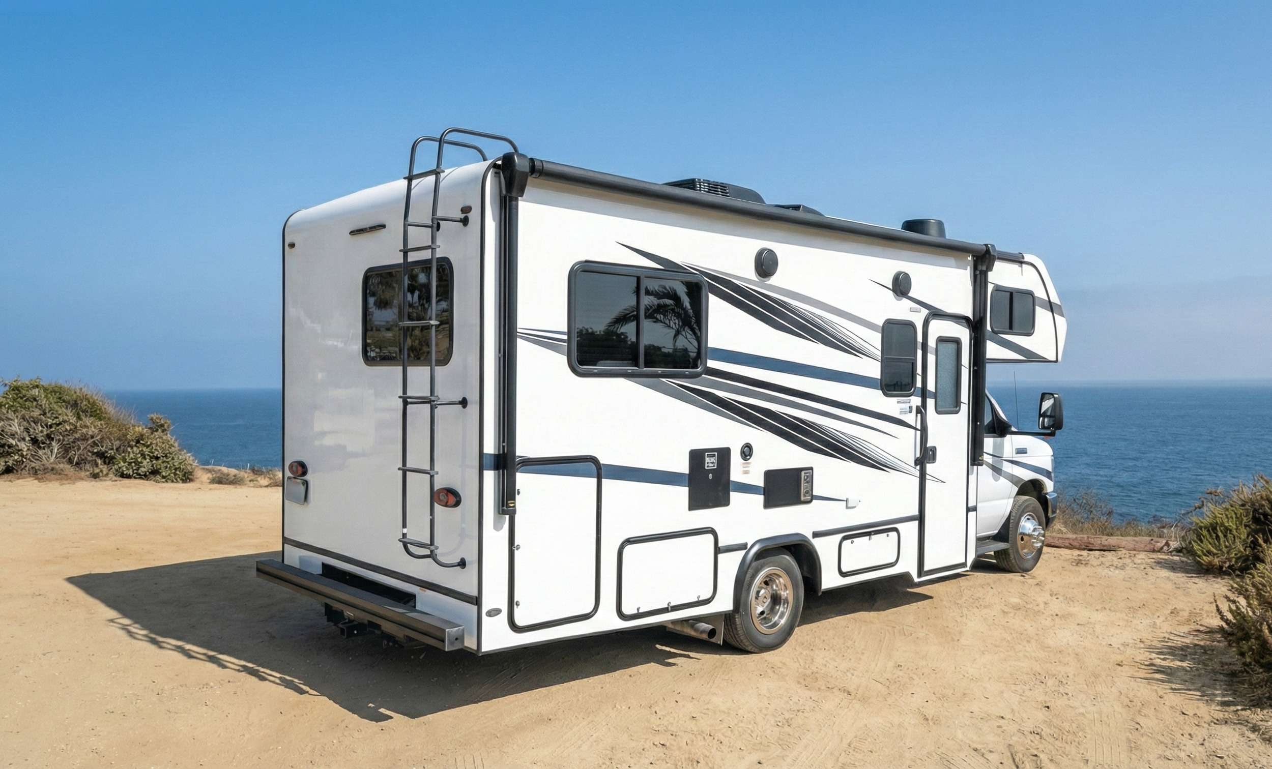 Casa rodante blanca estacionada en la playa con vista al mar y cielo despejado.