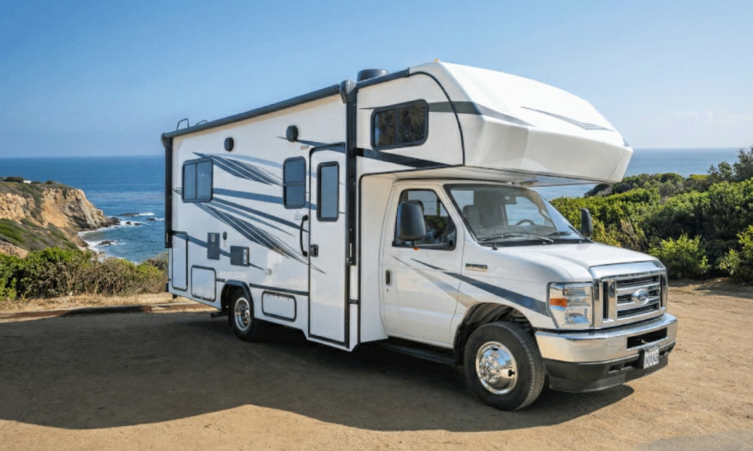 Camioneta recreacional blanca estacionada en un paisaje costero con vista al mar y colinas verdes.