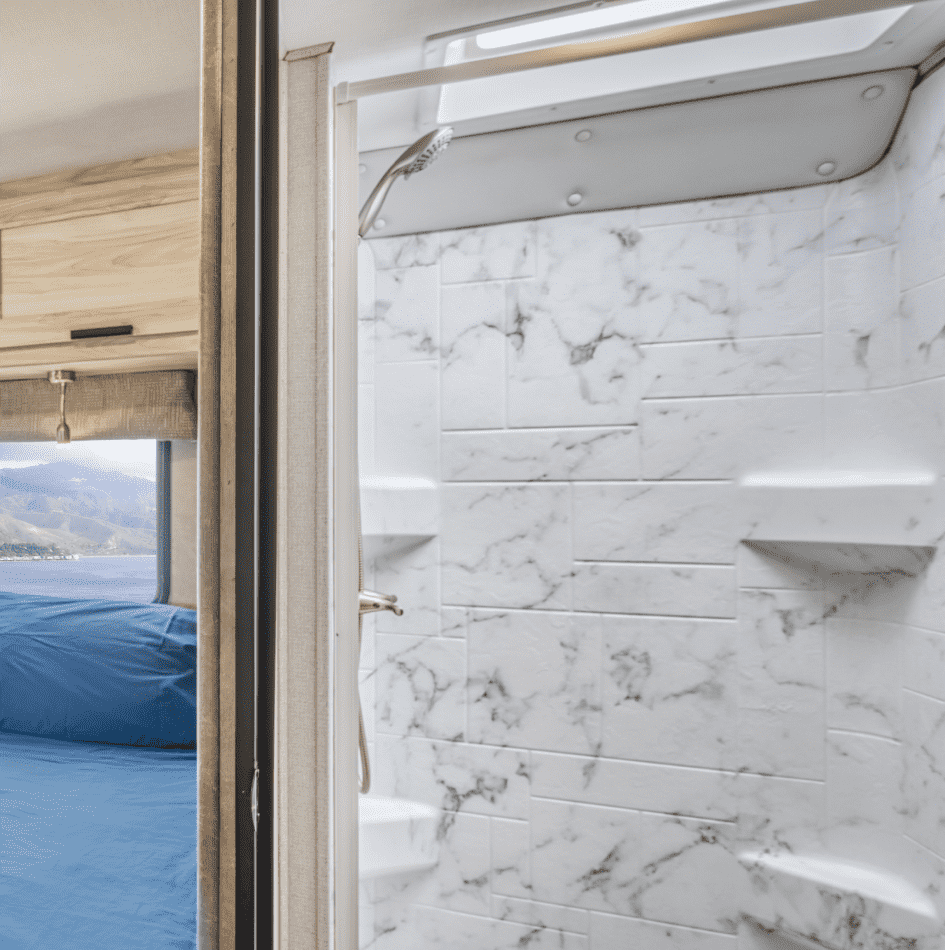 Ducha con paredes de mármol y ducha de lluvia en un espacio compacto de baño.