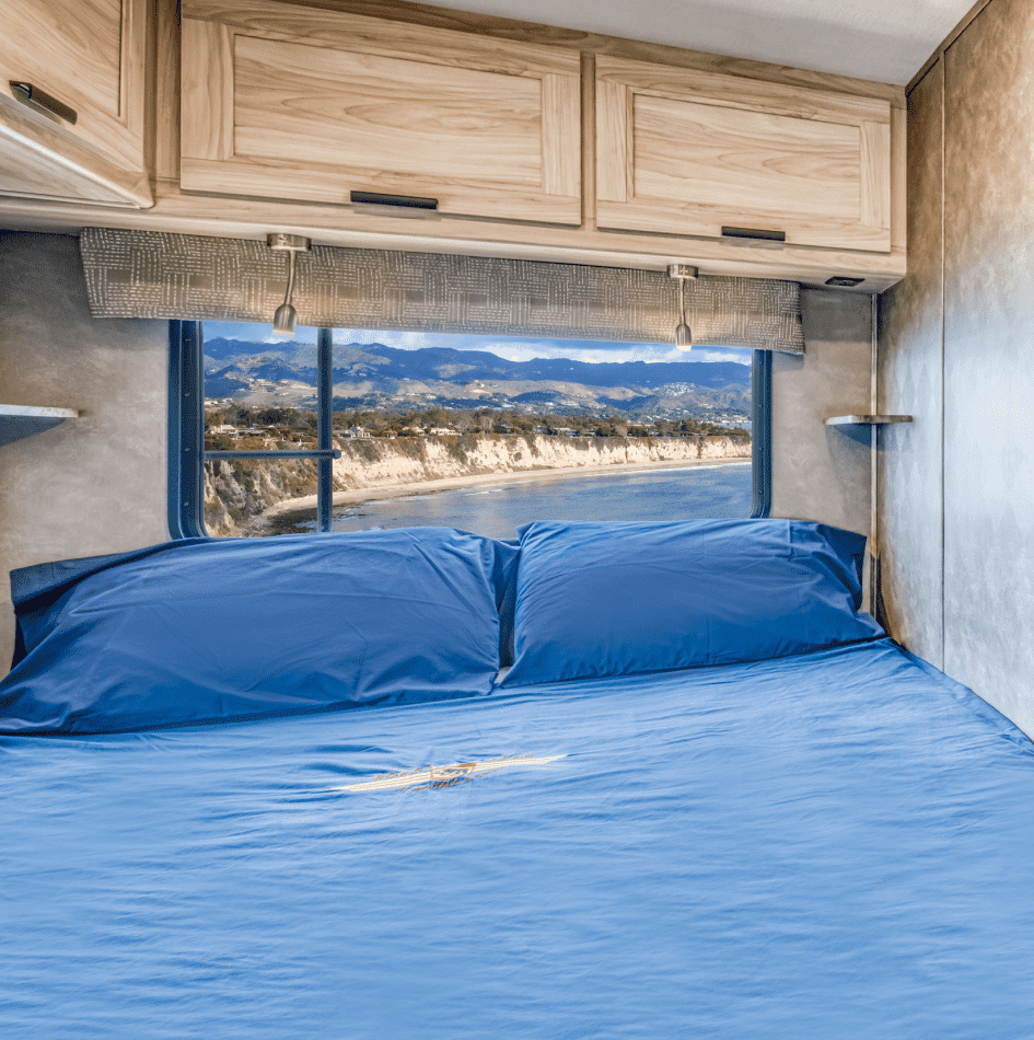 Cama con sábanas azules en una habitación con vista al mar y montañas a través de la ventana