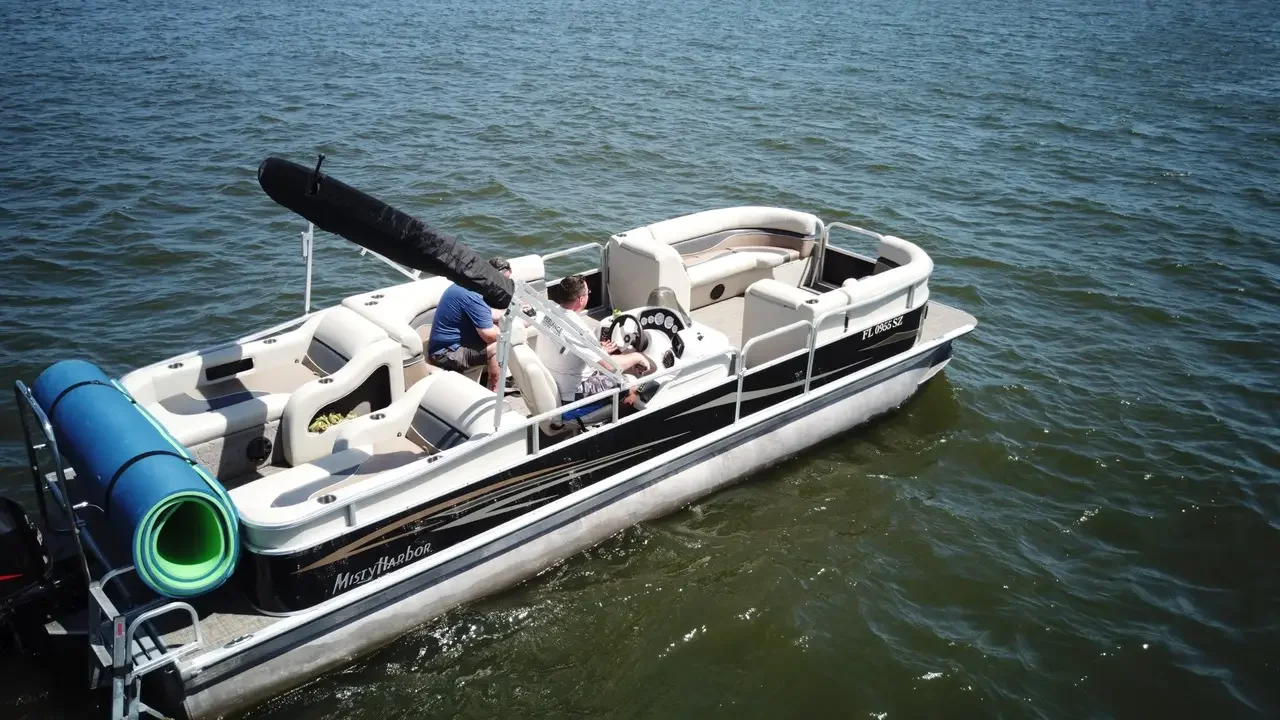 Bote de recreo en el agua con dos personas a bordo, una de ellas en el asiento de control y otra cercana a las sillas, con equipo de navegación y objetos de ocio.