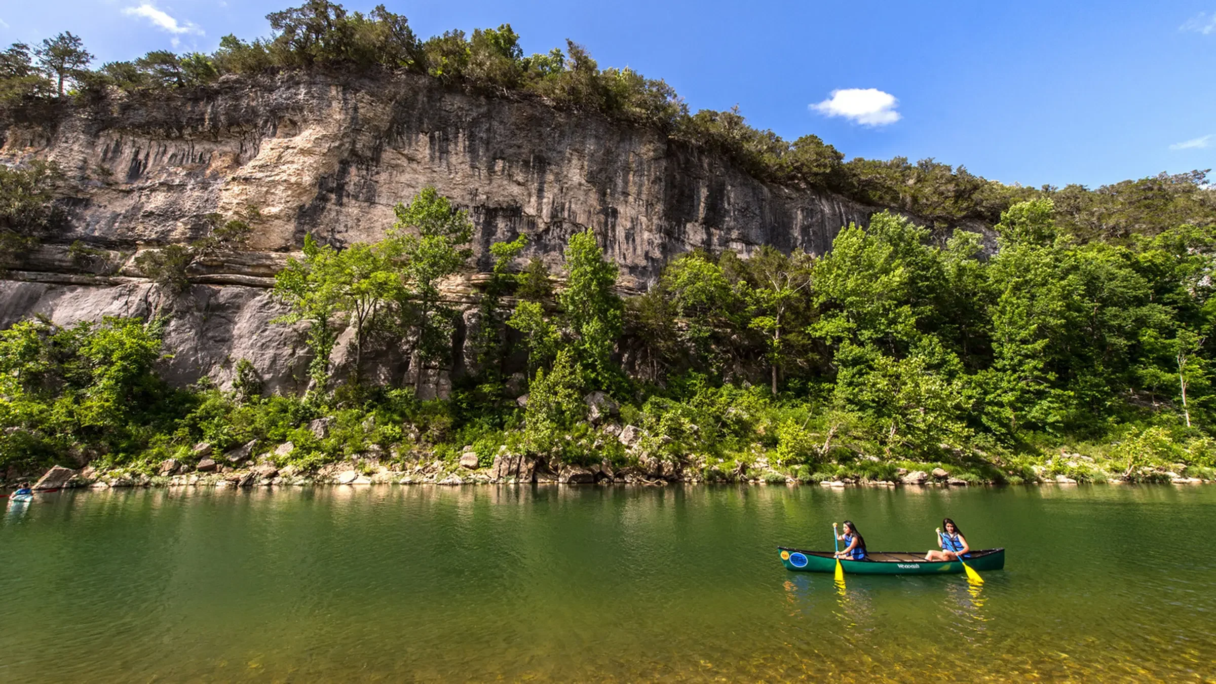 Dos personas remando en kayak en un río rodeado de vegetación y acantilados.