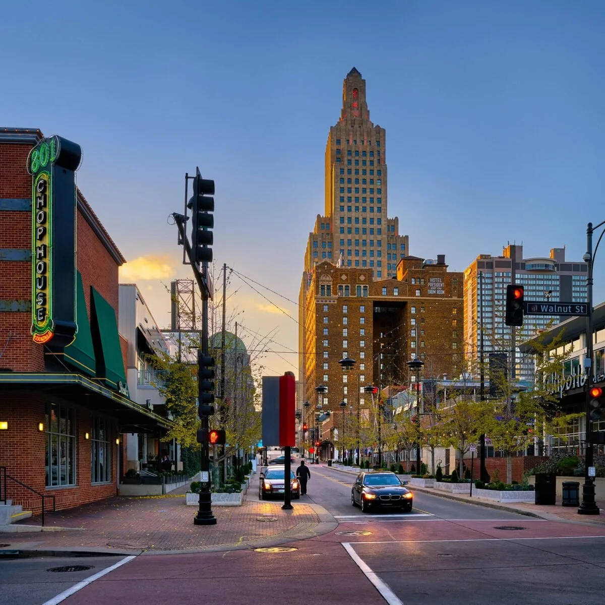 Vista urbana al atardecer en downtown con edificios altos, tráfico y árboles en la calle Walnut.