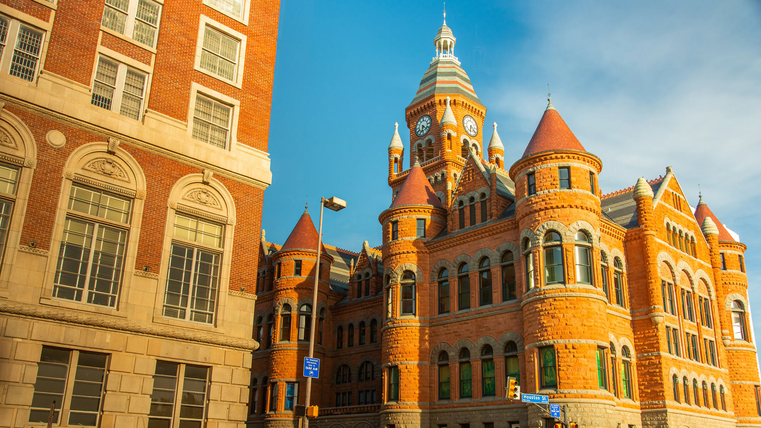Edificio antiguo de estilo gótico con torres y reloj, de color ladrillo, en una ciudad bajo cielo despejado.