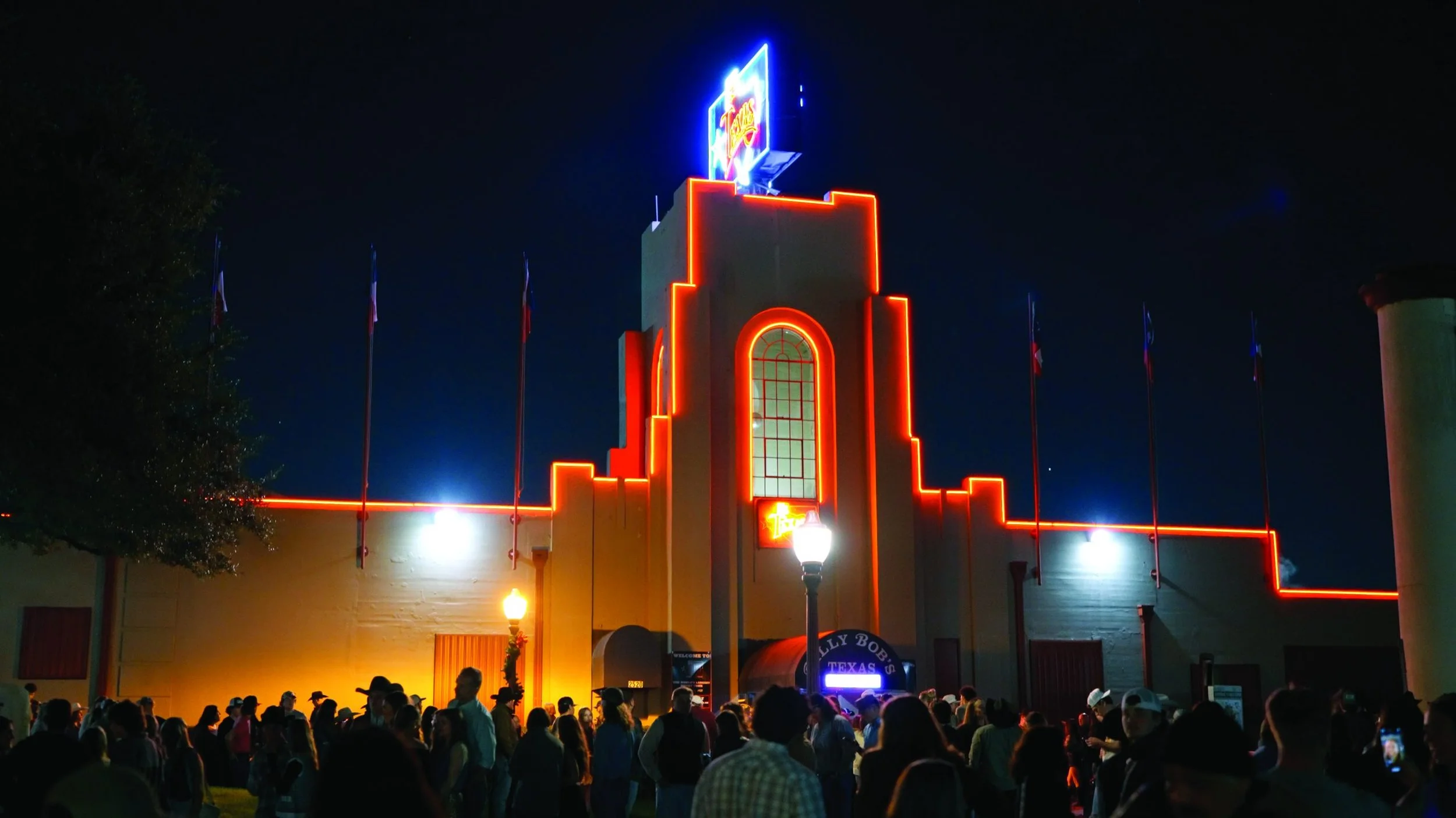 Fachada del teatro Billy Bob's Texas iluminada con luces de neón rojas y azules en la noche, con muchas personas reunidas frente a la entrada.