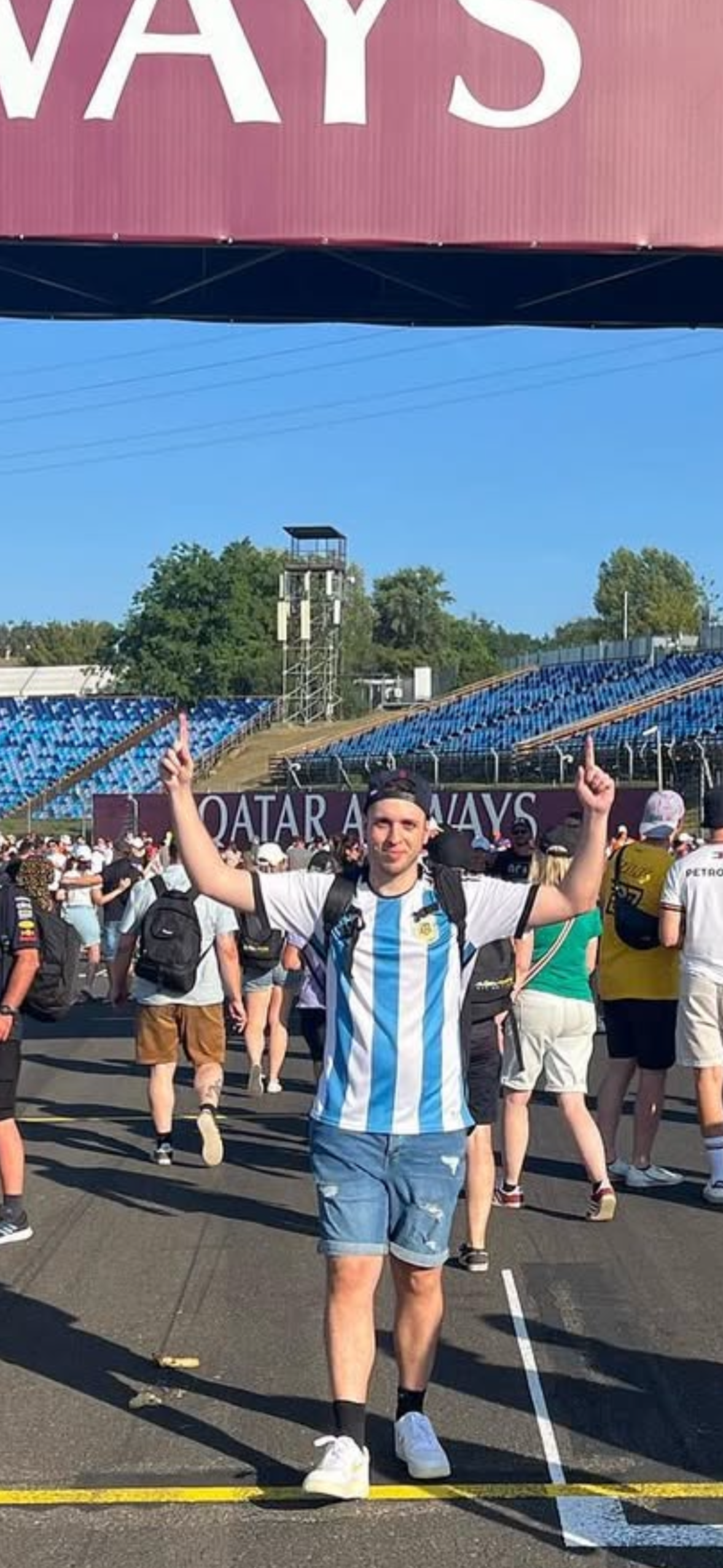 Un joven con camiseta de Argentina y pantalones cortos en un evento deportivo en un estadio con muchos espectadores y estructuras en el fondo.