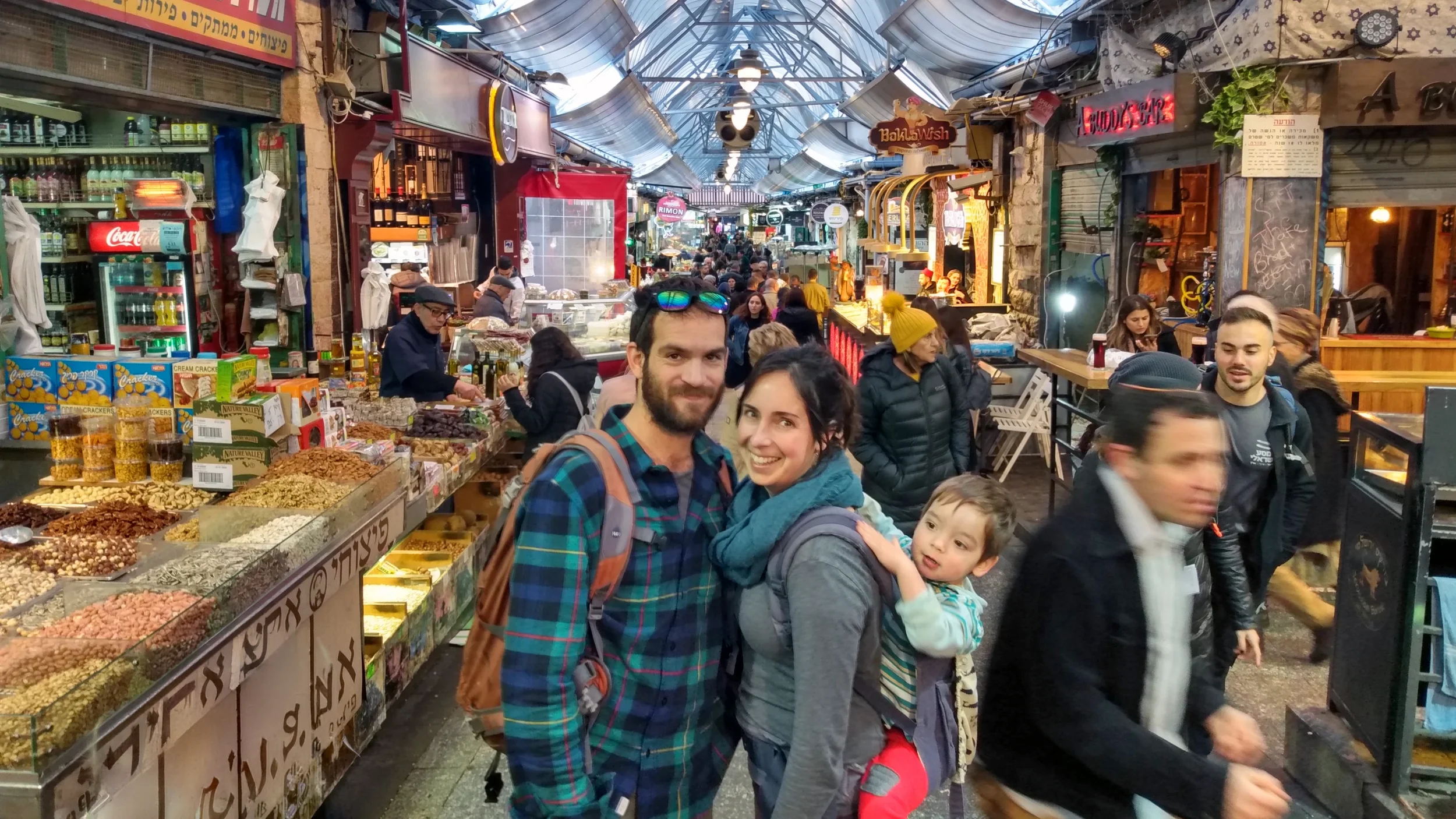A group of people shopping and exploring a busy, covered marketplace with various food stalls and vendors.