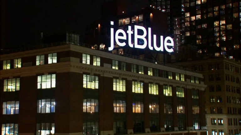Nighttime cityscape with a large illuminated JetBlue sign on top of a building.