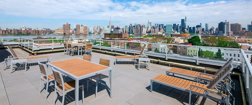 Rooftop terrace with outdoor tables and chairs overlooking New York City skyline.