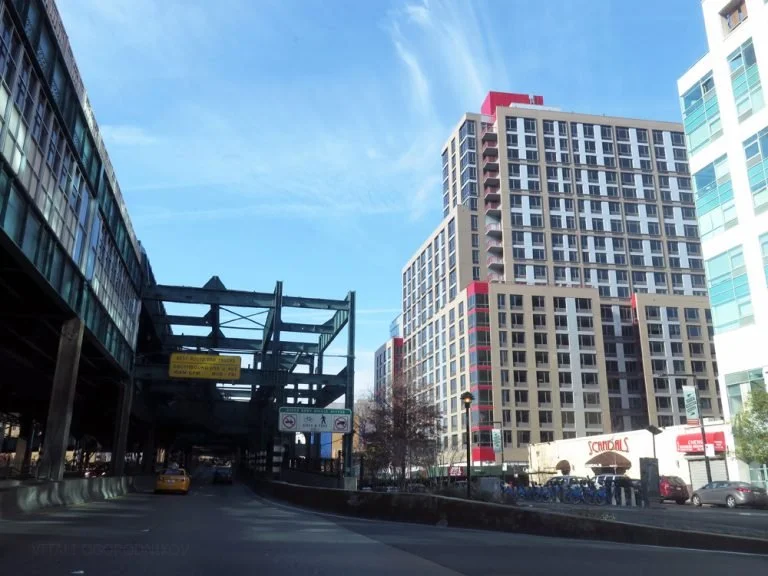 Tall modern buildings on a city street with a construction structure on the left and a parked taxi cab.