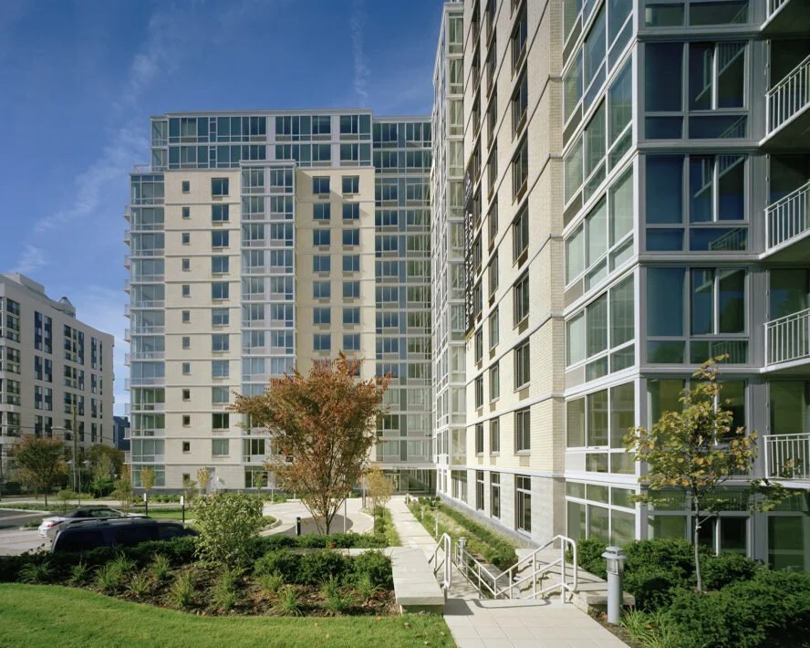 Modern high-rise apartment buildings with landscaped courtyard, trees, and pathways.
