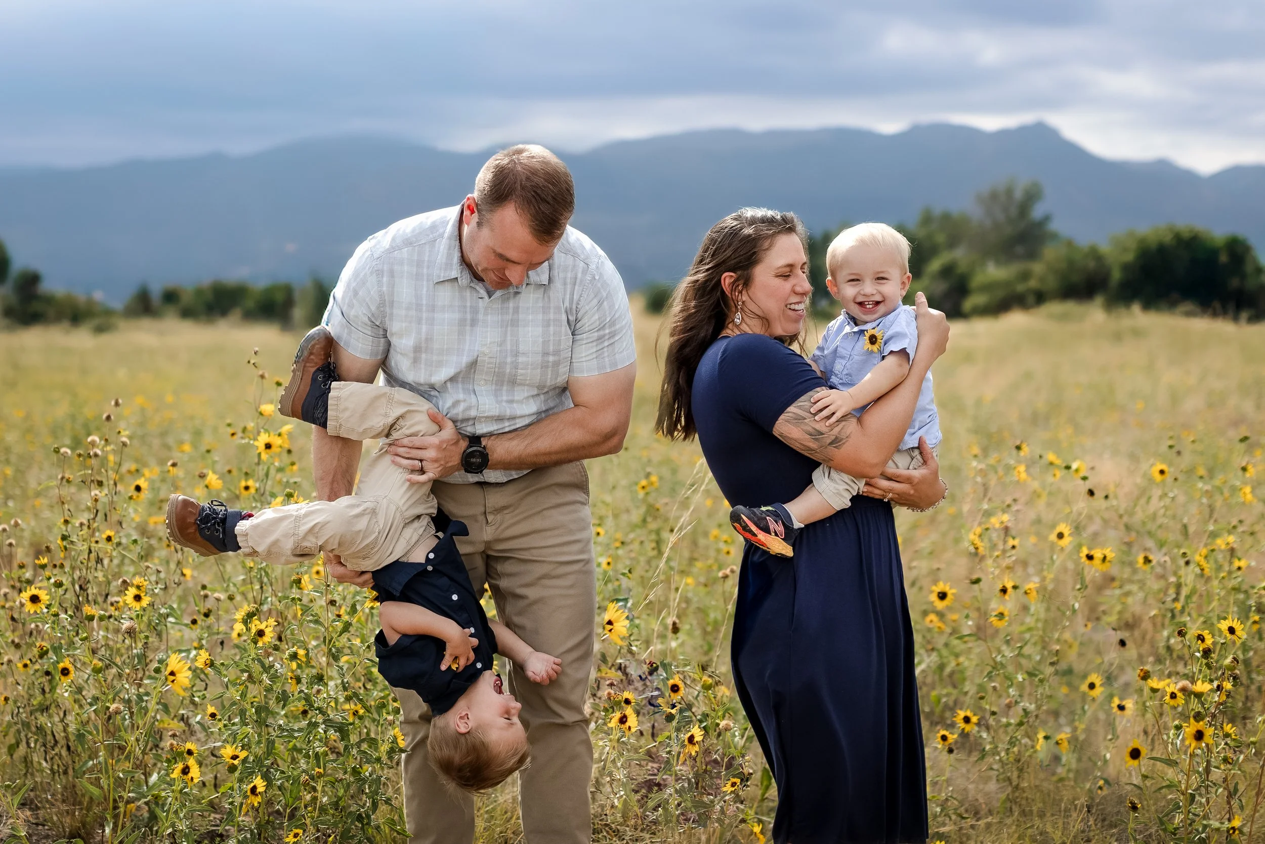 Family of four with their two toddlers in a beautiful sunflower field. Pikes Peak located in the background in beautiful Colorado Springs, Colorado. Lots of laughter in the huge sunflower field with giggles and playful moments.  