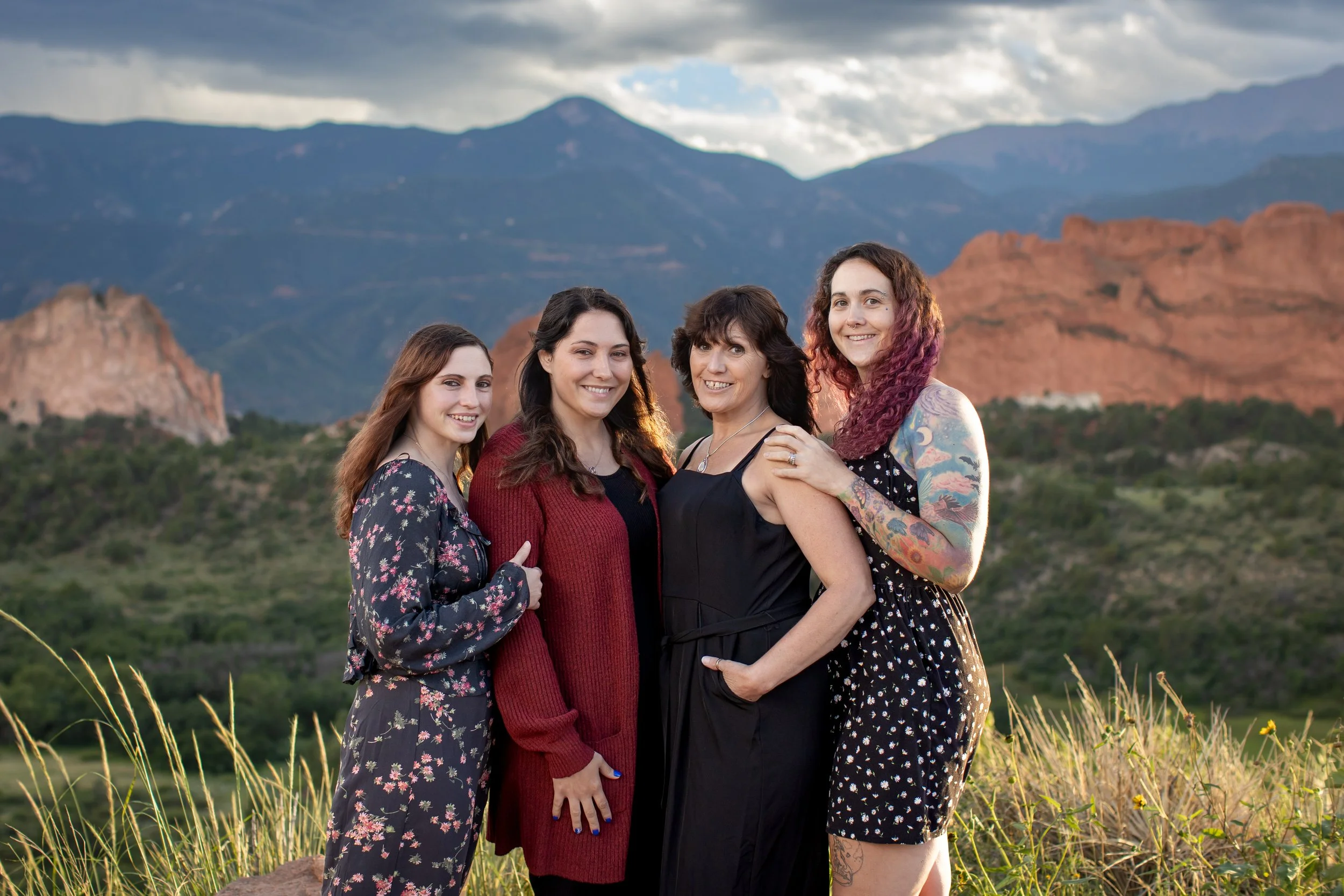 A mother and her adult daughters holding eachother close with the Garden of the Gods and Pikes Peak located in the background of the image. A beautiful sunset located in Colorado Springs, Colorado.  