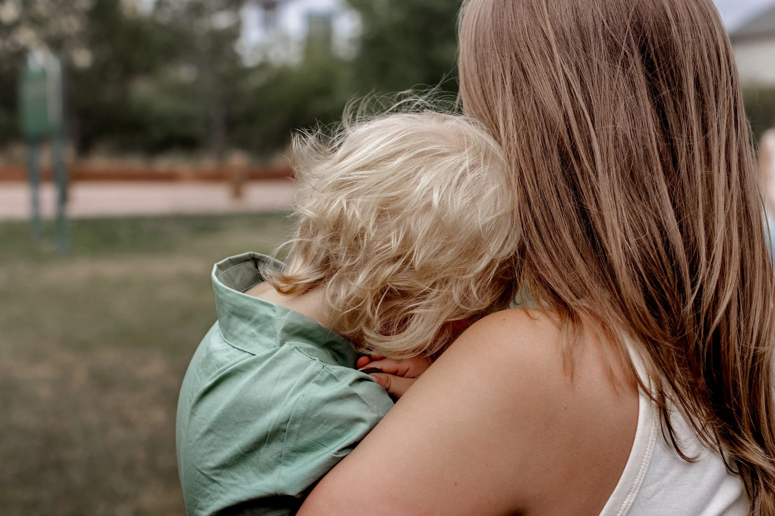 Toddler boy with bright blonde hair and curls snuggling on moms shoulder as they both enjoy the oudoors of Colorado Springs, Colorado's unpredictable weather. Looking away from the camera and brining in connection. 