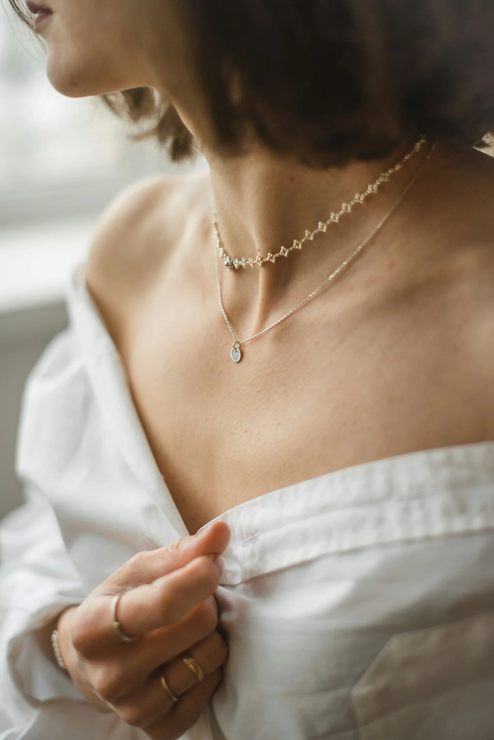 woman's chest with necklace stack and hand with rings