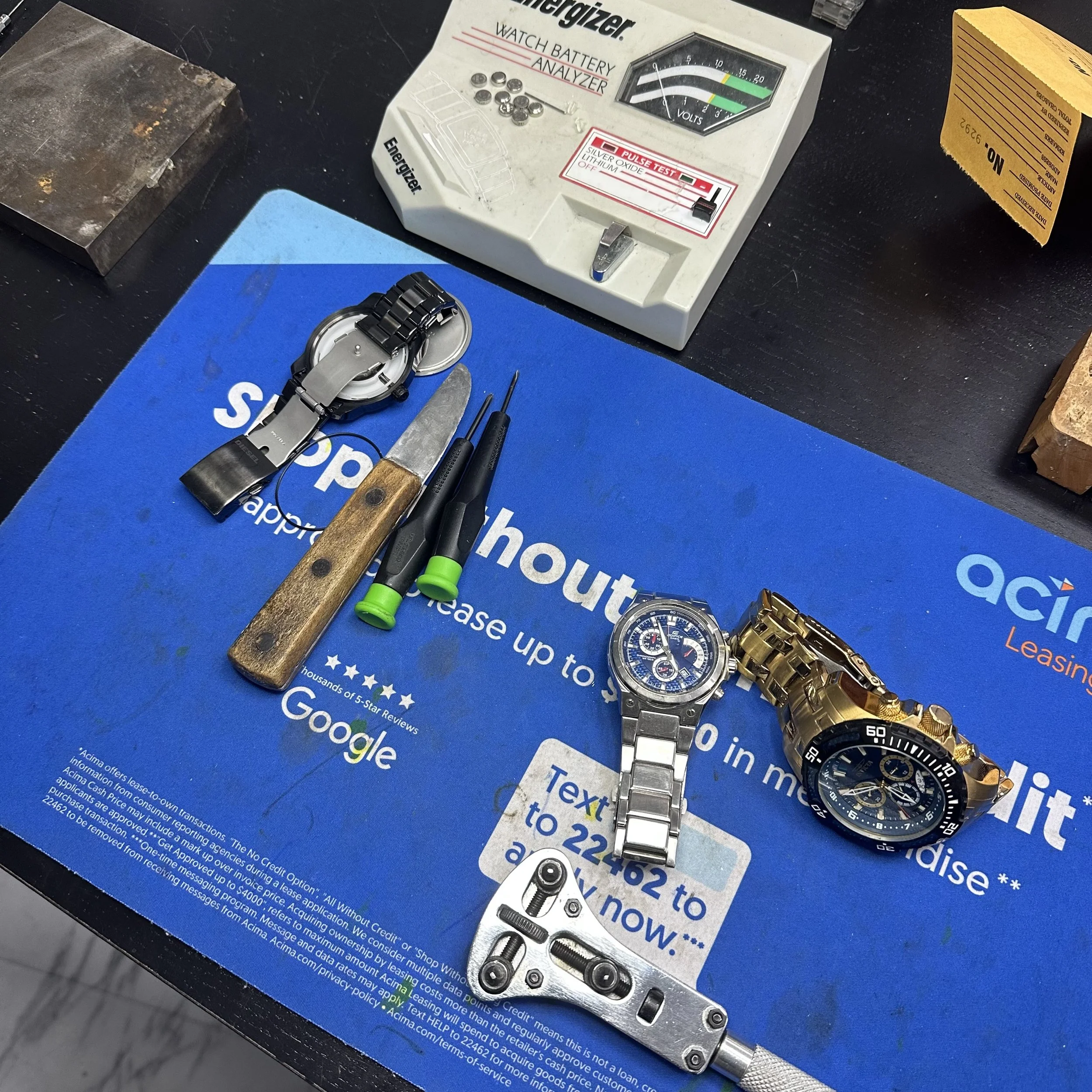 countertop with 2 watches and various watch battery replacement tools