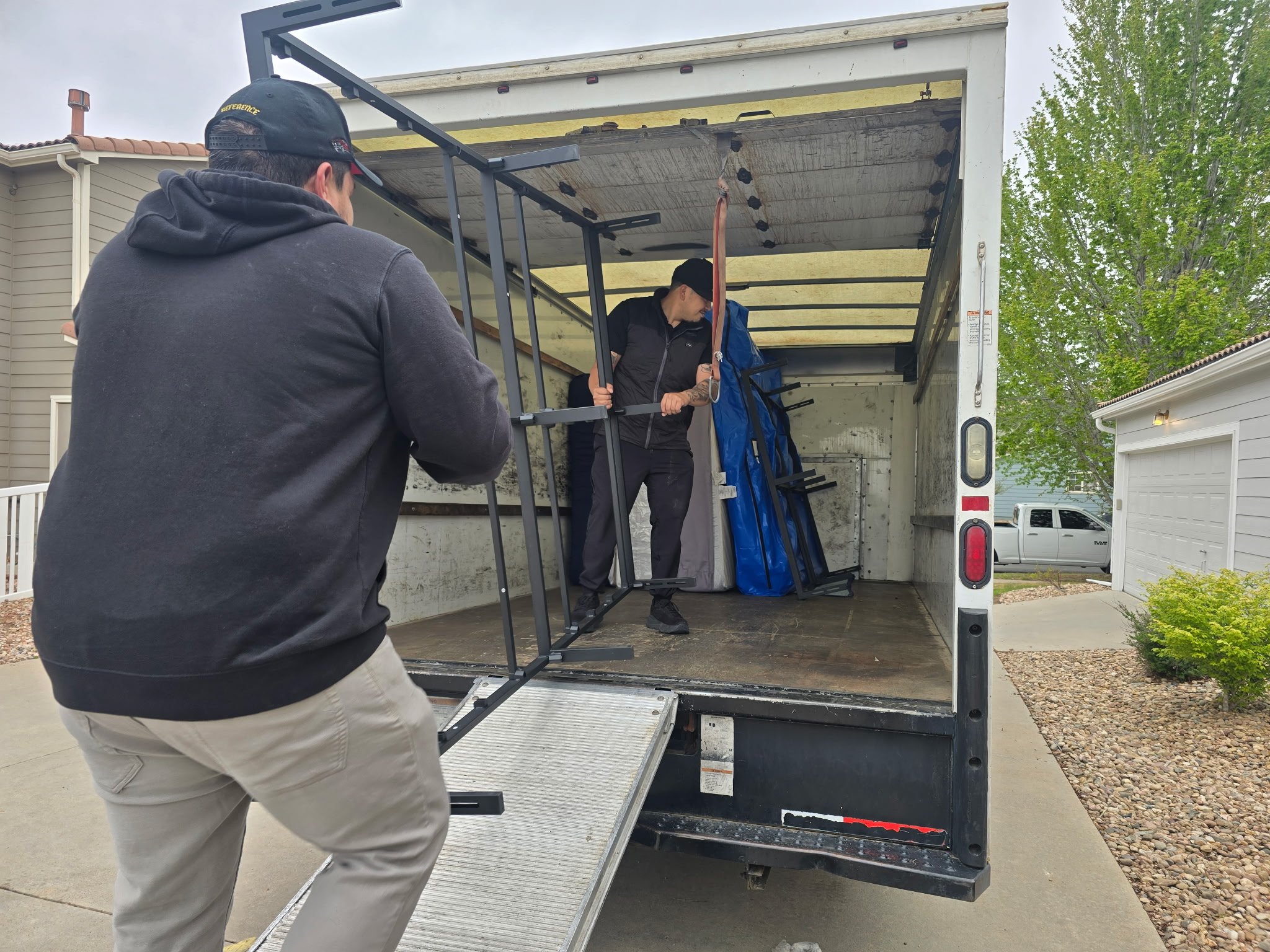 People unloading items from a moving truck with a ramp, outdoors in a residential area.