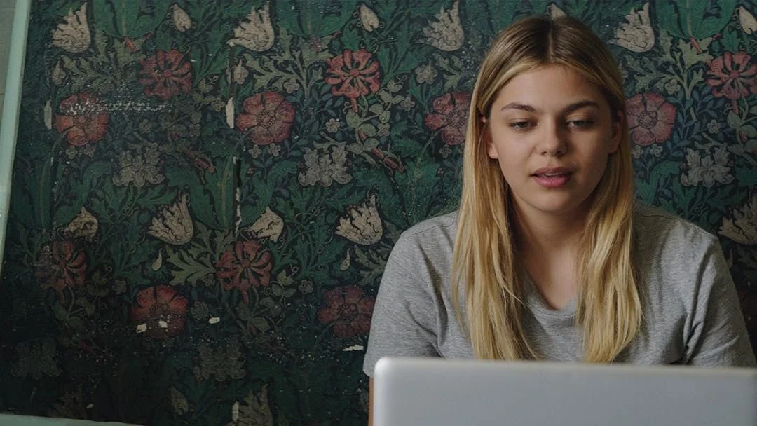 Jeune femme blonde utilisant un ordinateur portable dans un décor avec papier peint floral.