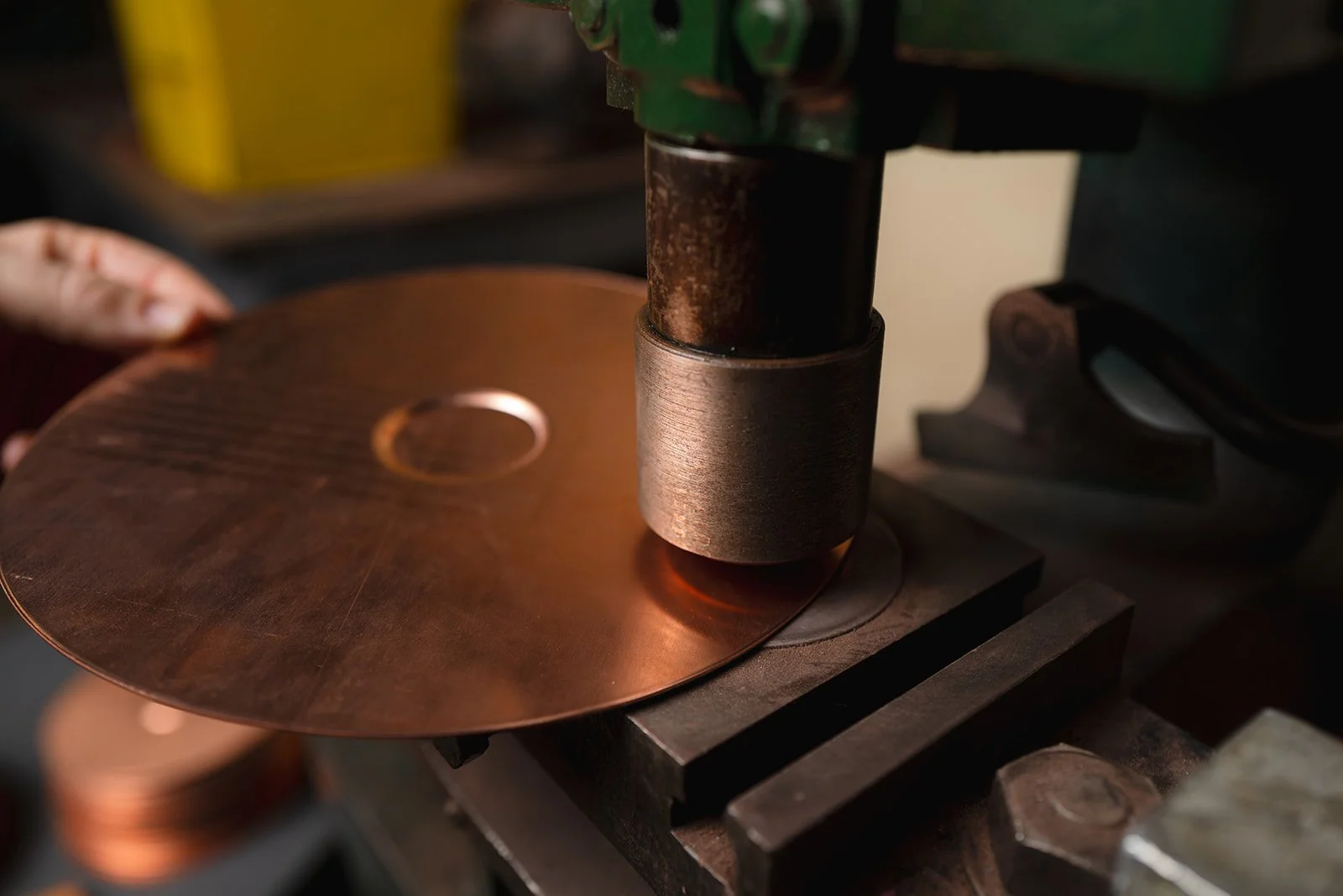 Close-up of a copper disc being pressed by a machine with a metal cylinder, part of an industrial manufacturing process.
