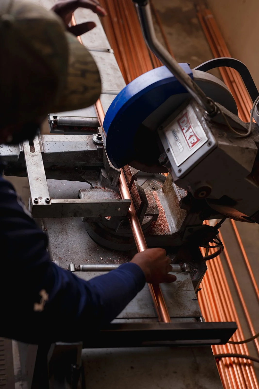 A person operating a pipe threading machine in a workshop, threading a copper pipe.