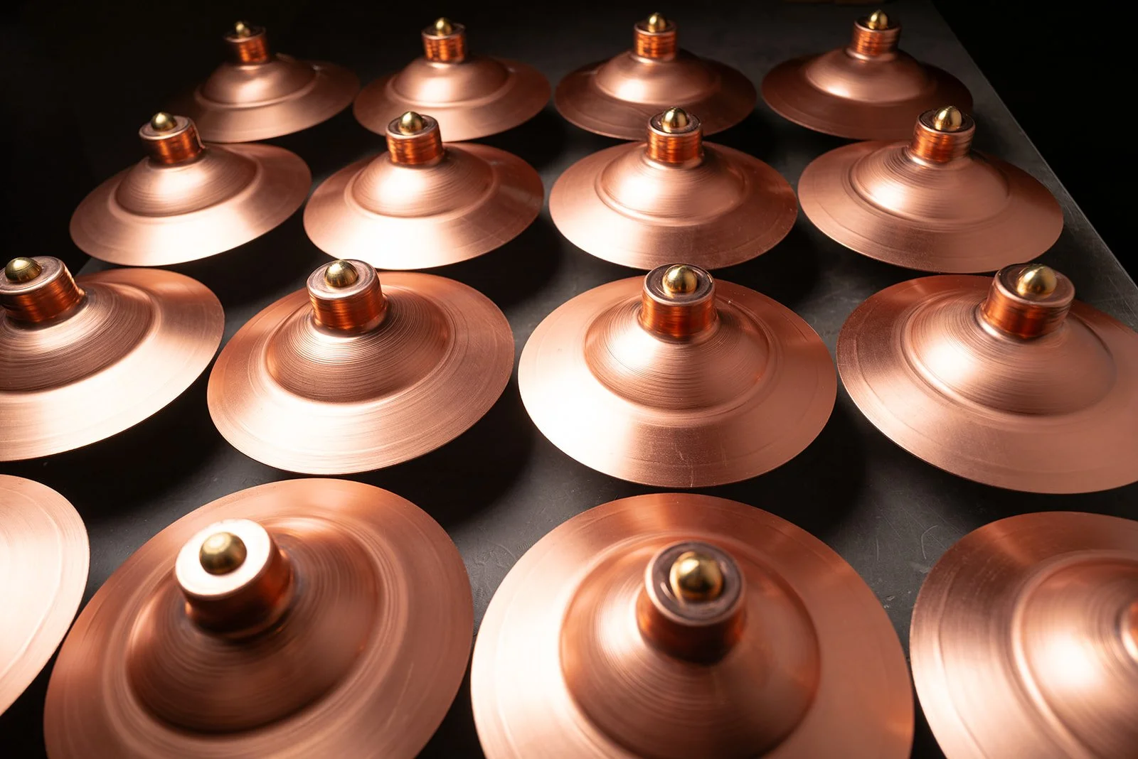 Multiple copper-colored metal spinning tops with shiny gold center caps arranged on a black surface.