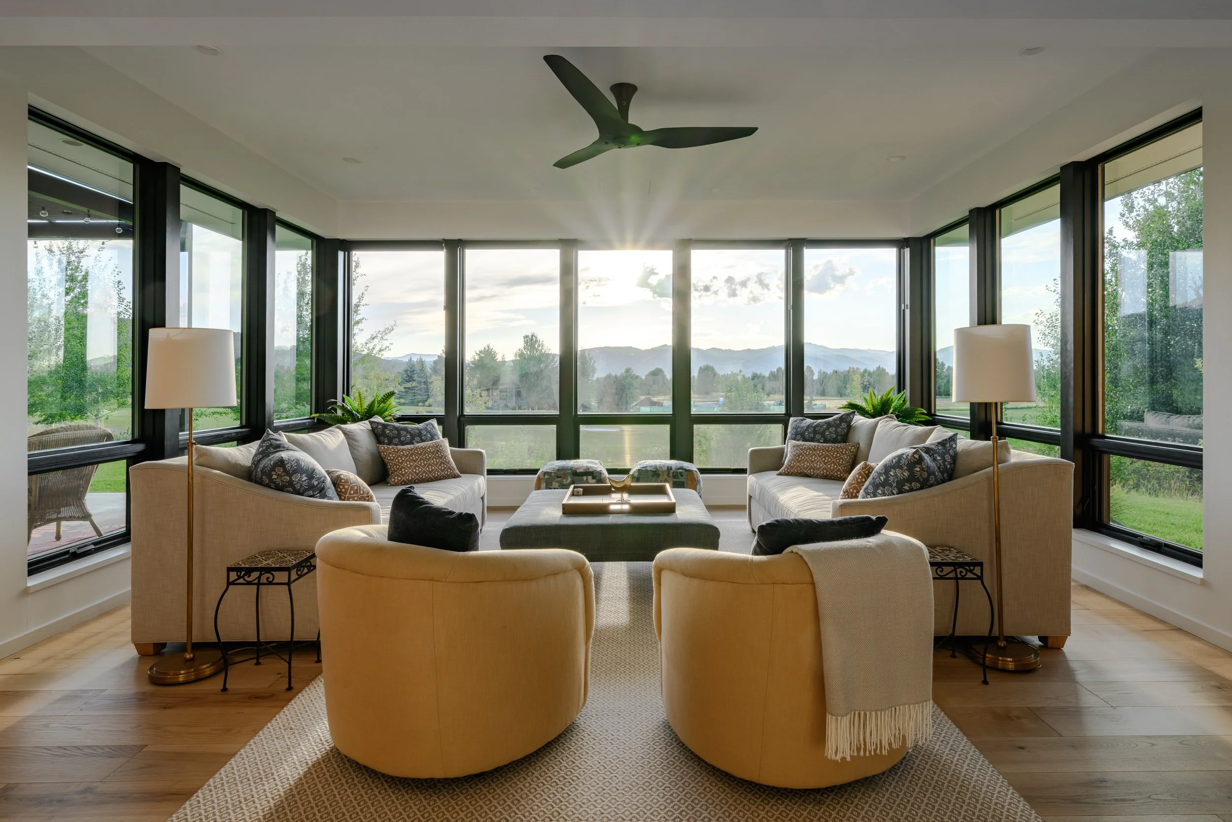 Living room with large windows, beige sofas, yellow armchairs, and a view of mountains and greenery outside.