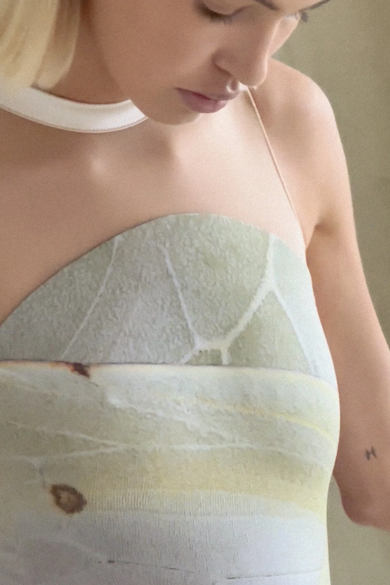 Close-up of a woman with a septum piercing, wearing a strapless top with a abstract pattern of green, beige, and white colors.