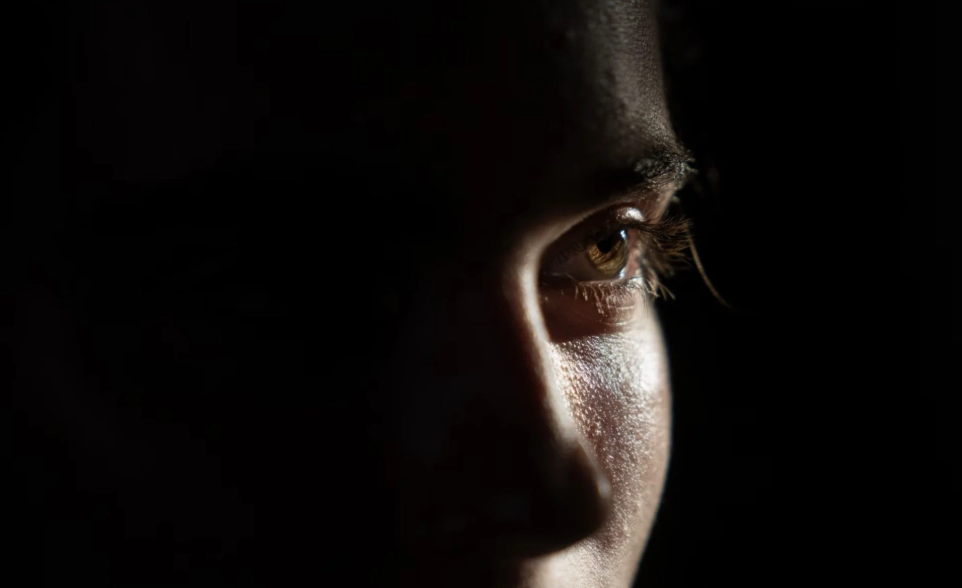 Close-up of a person's face, focusing on the right eye, illuminated by light against a dark background.