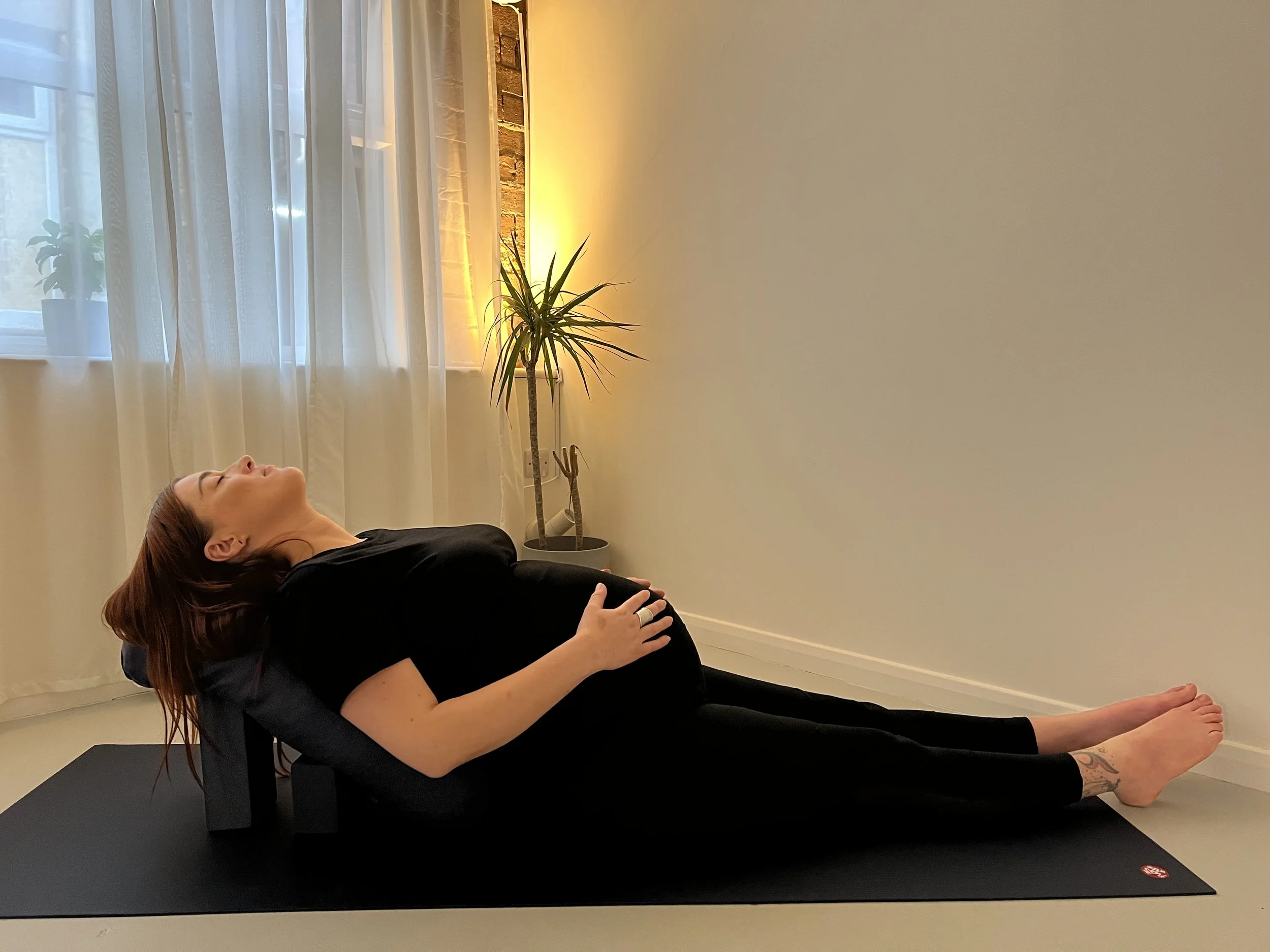 Melanie laid on yoga mat with bolster cushion support holding bump with relaxed expression