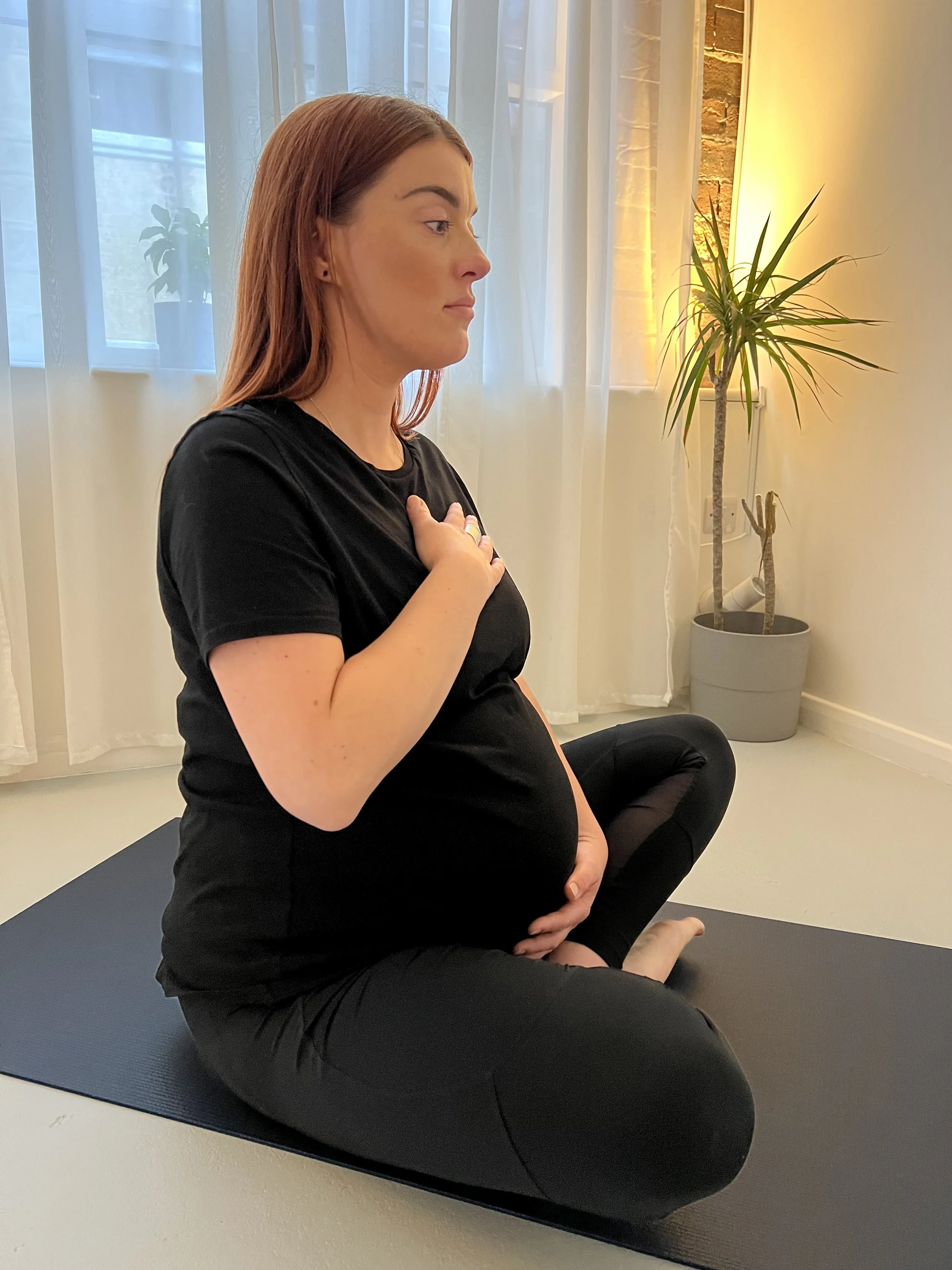 Melanie pregnant on yoga mat with one hand on heart and one on baby bump