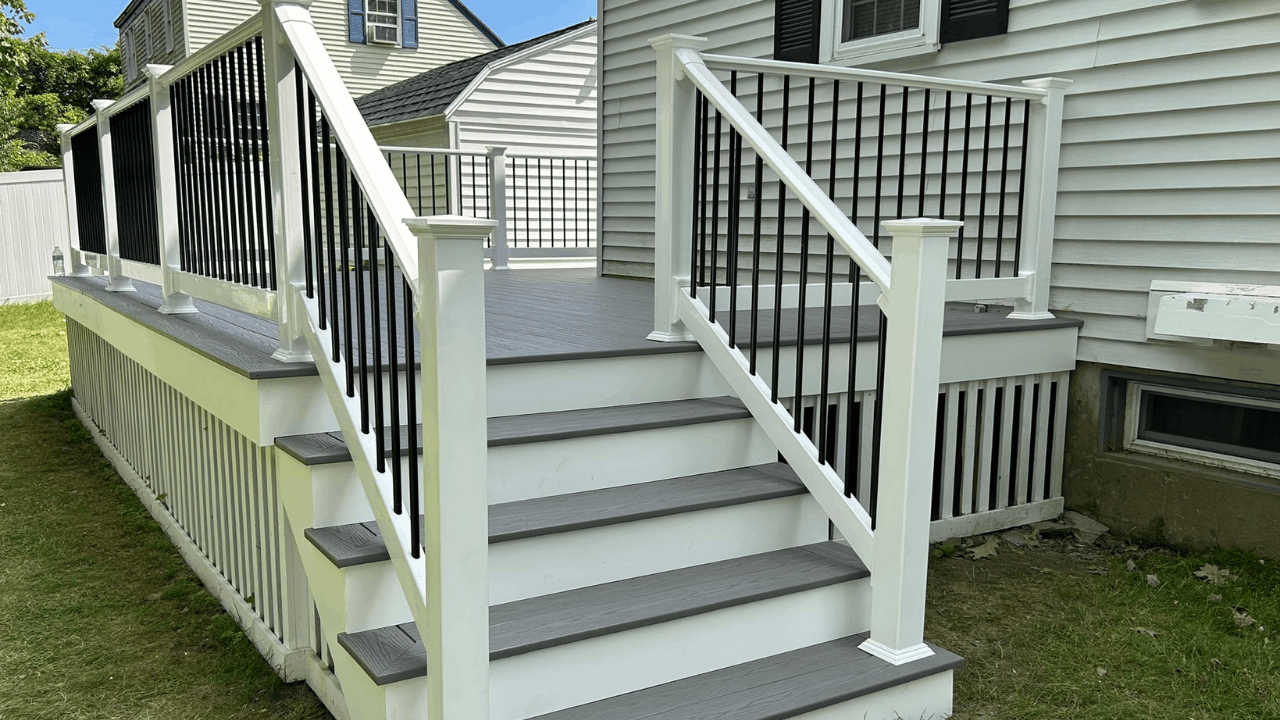 New gray wooden porch stairs with black metal railing and white support posts leading up to a house with white siding.