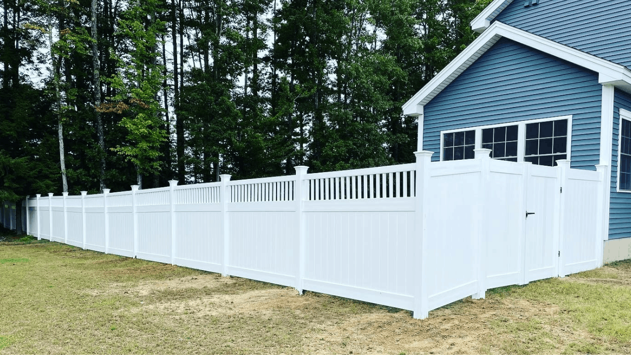 White privacy fence around a backyard with green trees behind it, next to a blue house with white trim and multiple windows.