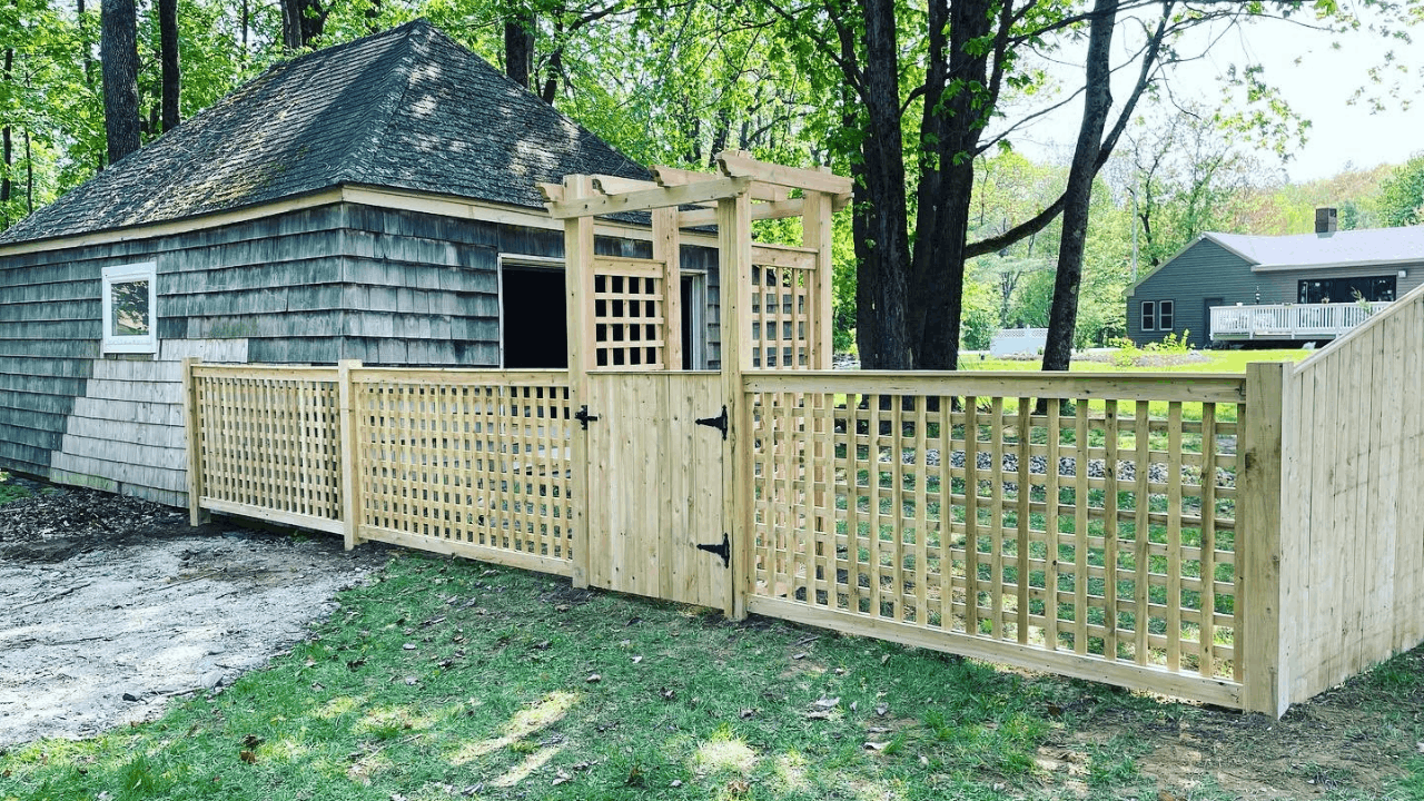 Wooden enclosure with a gate, installed next to a small shed in a backyard surrounded by trees and other houses in the background.