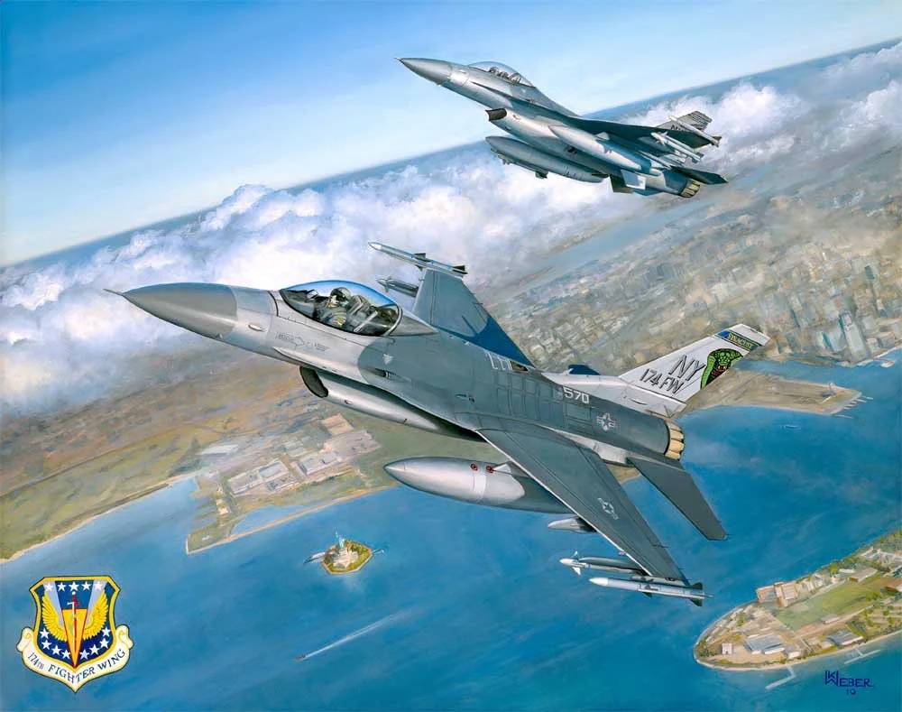 Two fighter jets flying above water and land, with a cityscape in the background. The jets are military aircraft, one with a shark mouth nose art and the other with a snake on the tail. There is a badge of the 174th Fighter Wing on the bottom left co