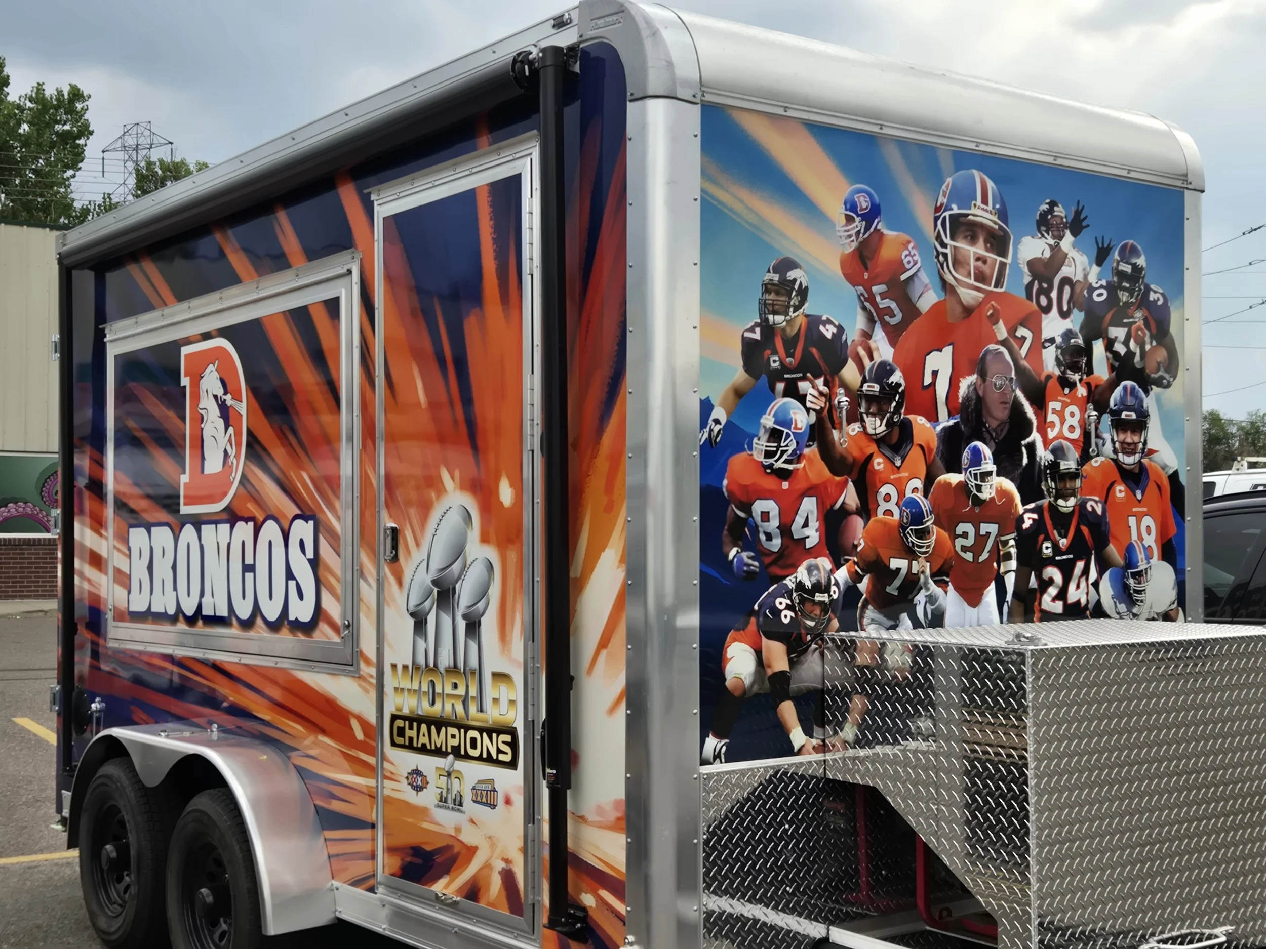 A Denver Broncos team trailer decorated with Broncos players and a Super Bowl logo, celebrating their 50th Super Bowl win.