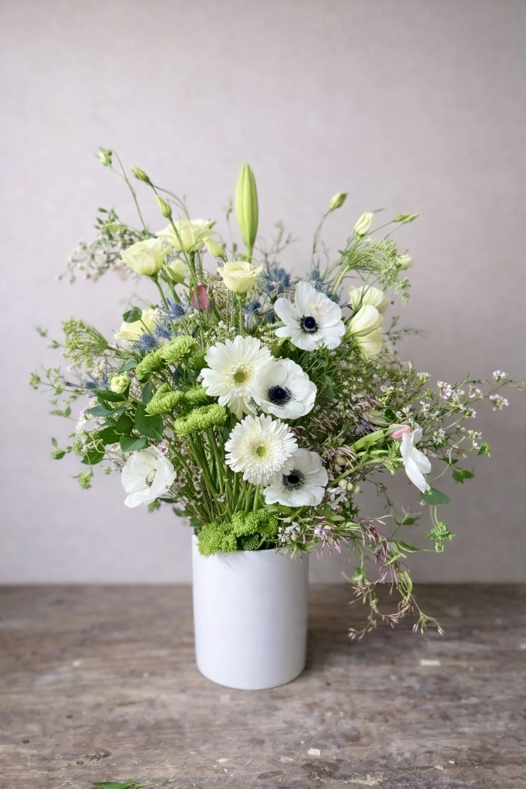 A bouquet of white and green flowers in a white vase on a wooden surface.