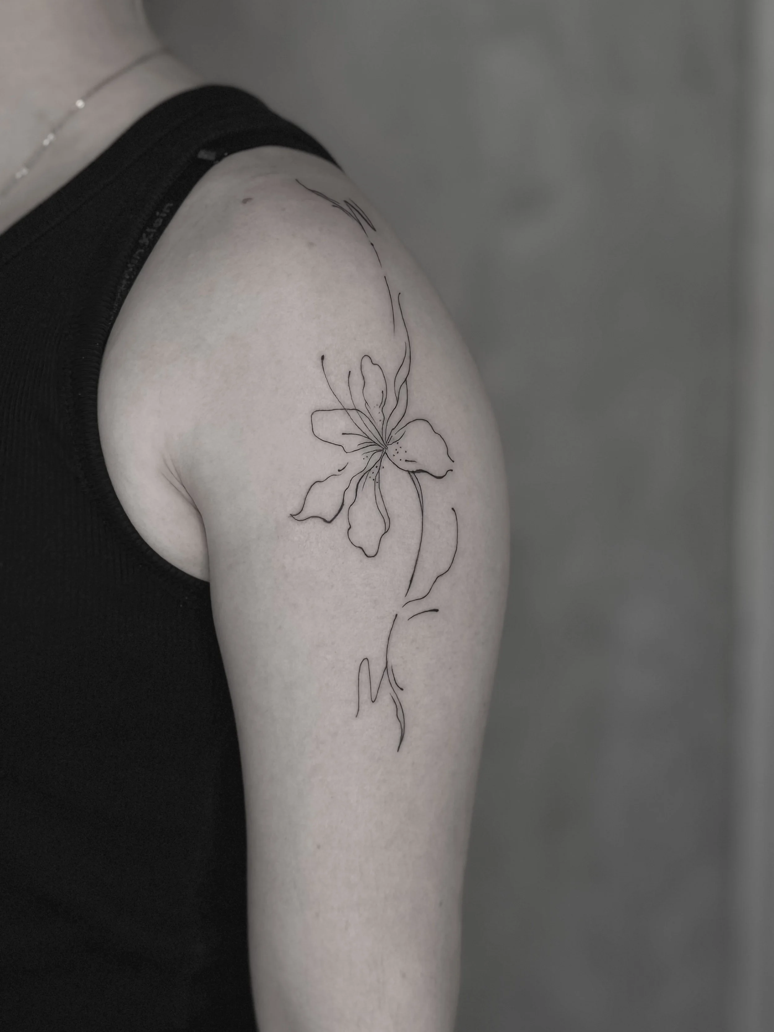 Black ink floral tattoo on person's upper arm, featuring a large flower with detailed petals and leaves.