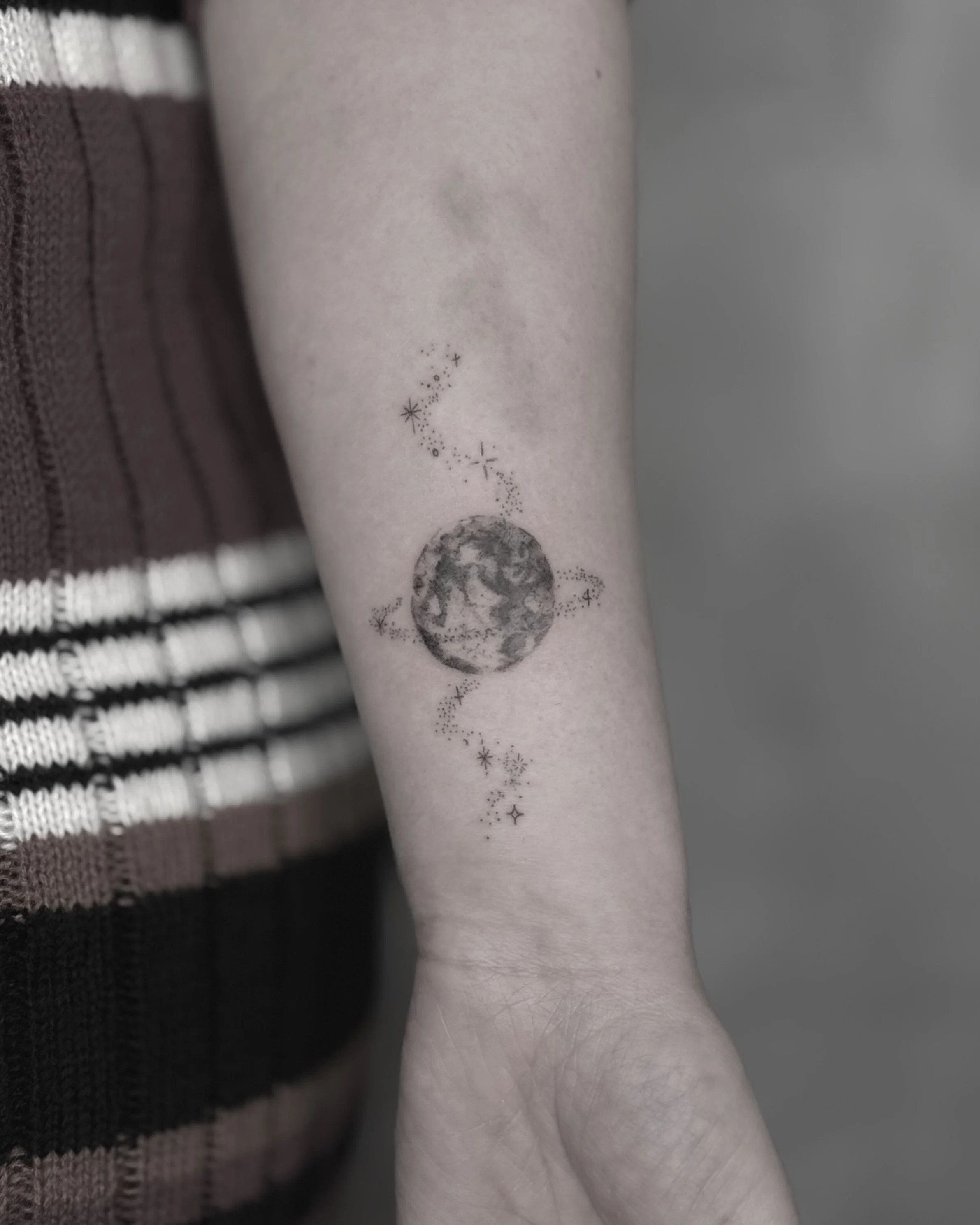 Tattoo of the moon with stars and dotted lines on person's forearm.