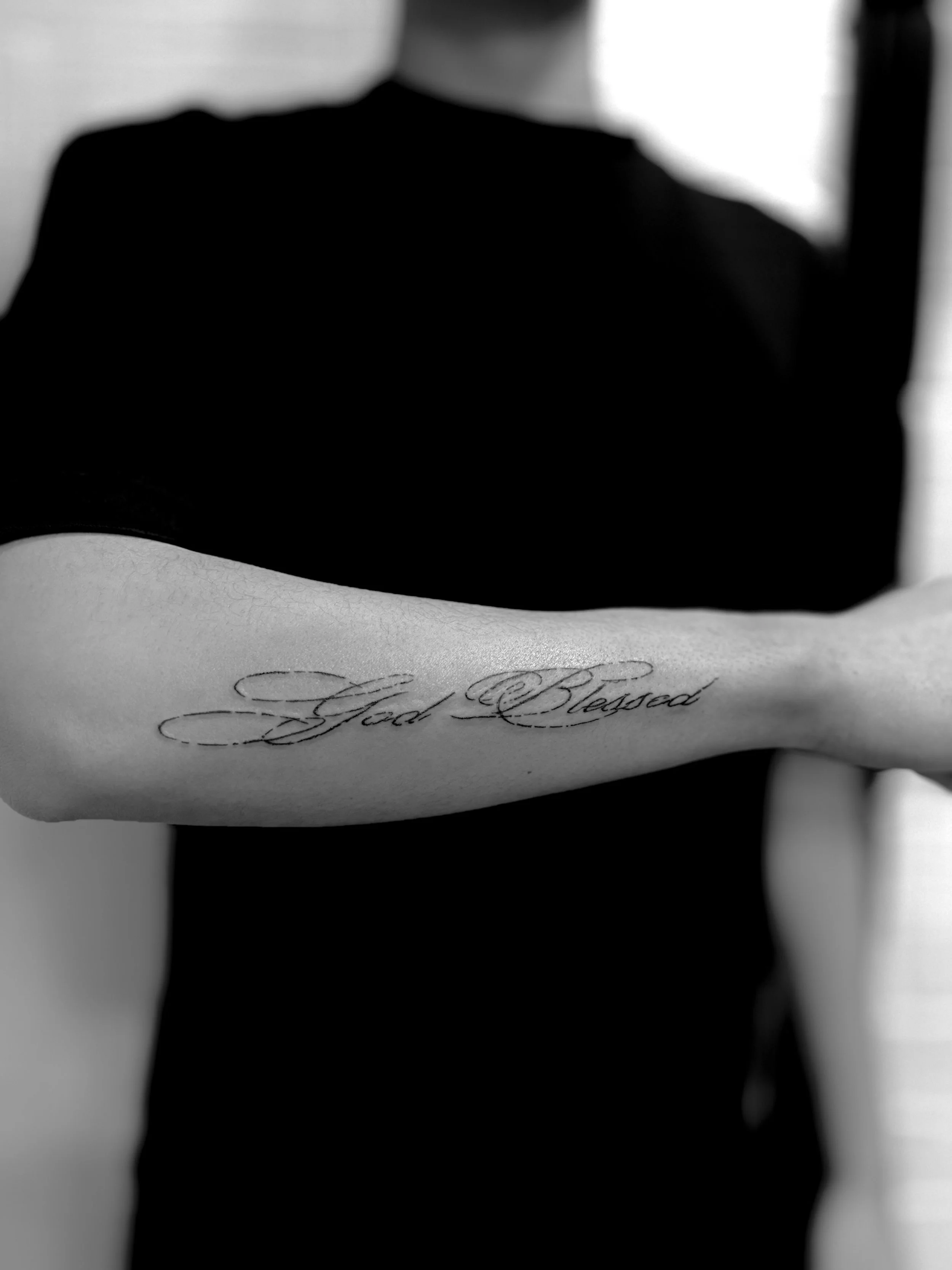 A person's arm with a tattoo that says 'God Blessed' in cursive script.