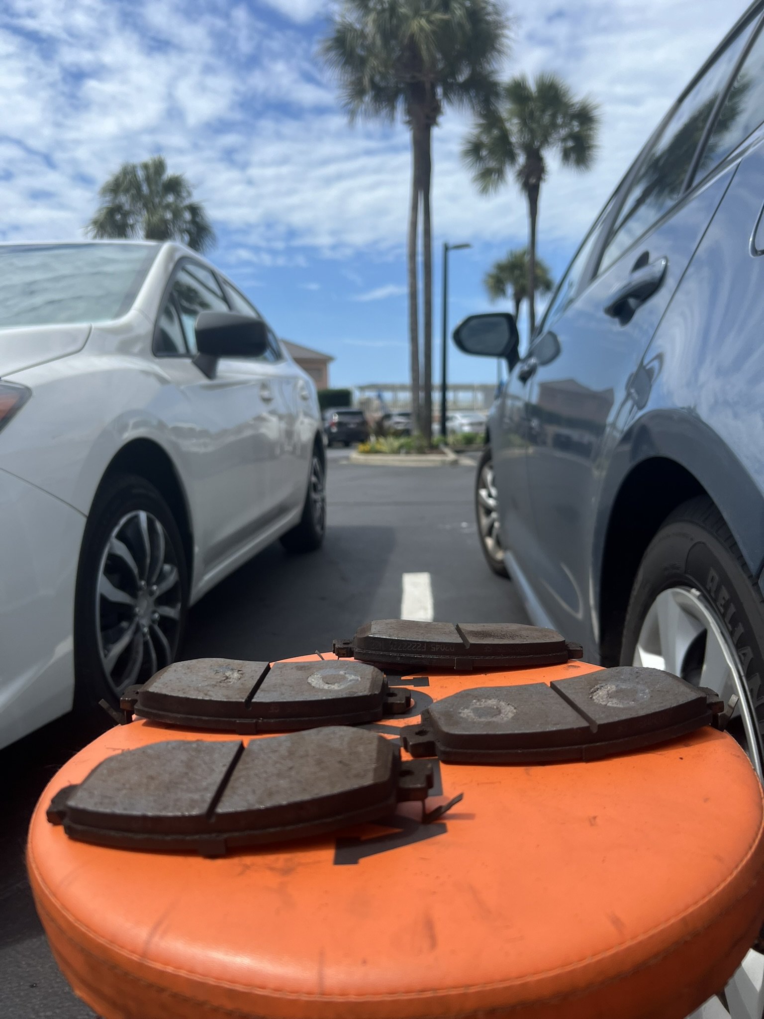 Close-up of brake pads on an orange seat with cars and Florida palm trees in the background.