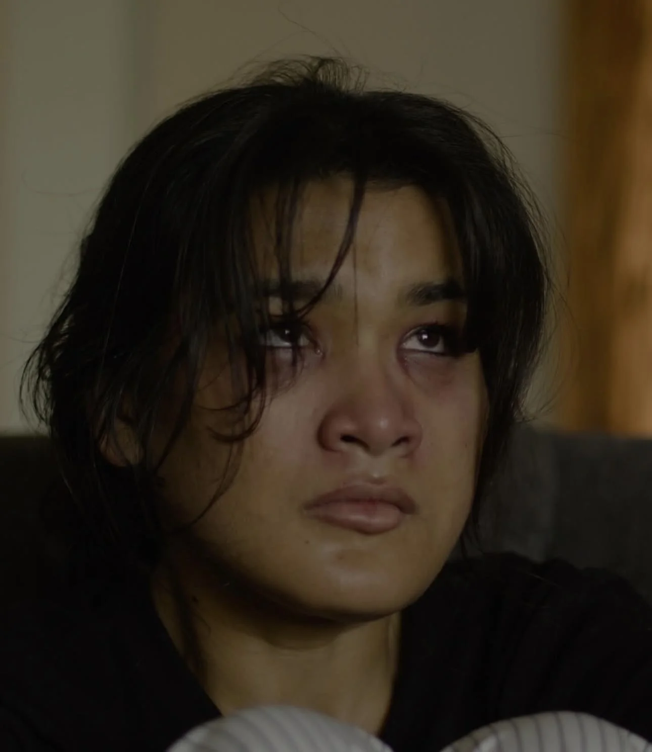 A woman with wet hair and a distressed expression, sitting with her eyes rolled back and tears in her eyes.