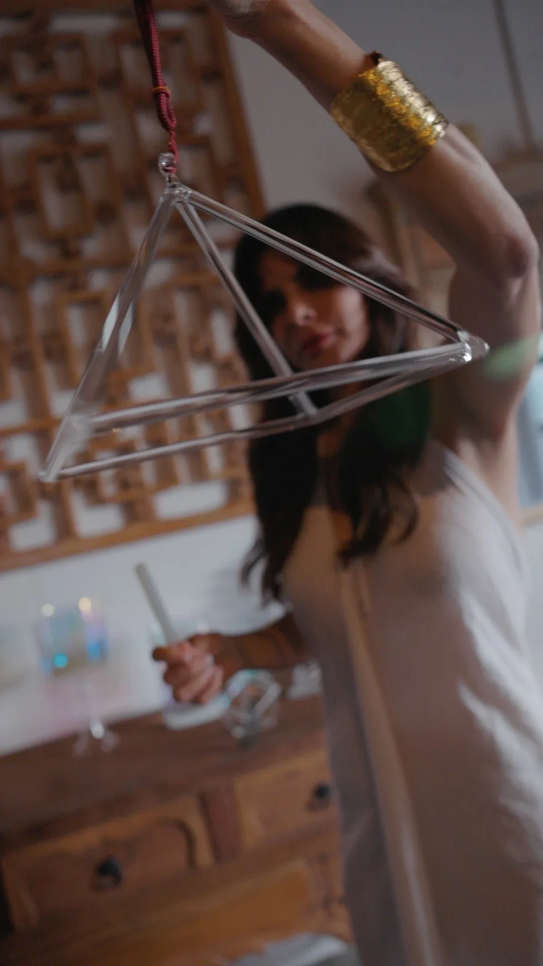 A person holding a triangle-shaped glass piece on a red string, with another person in the background holding a smartphone.