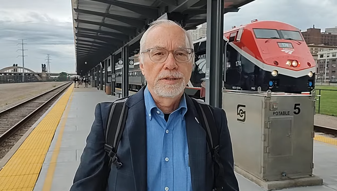 Scott standing at a train station with a red Borealis train engine in the background.