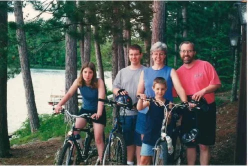 Scott, his wife, Shirley and his three children smiling at the camera. They are standing with bikes in the woods.
